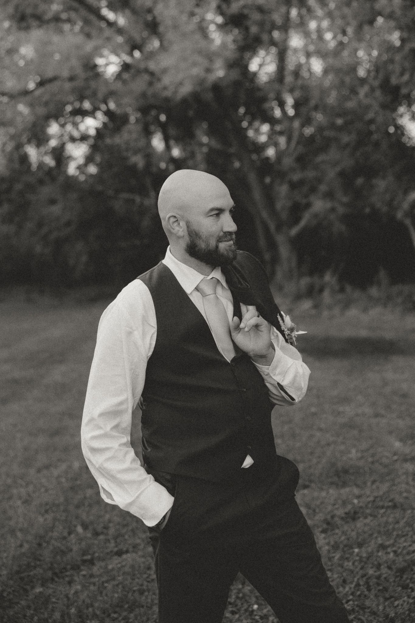 Side profile portrait of person in formal vest and white shirt against natural outdoor setting.