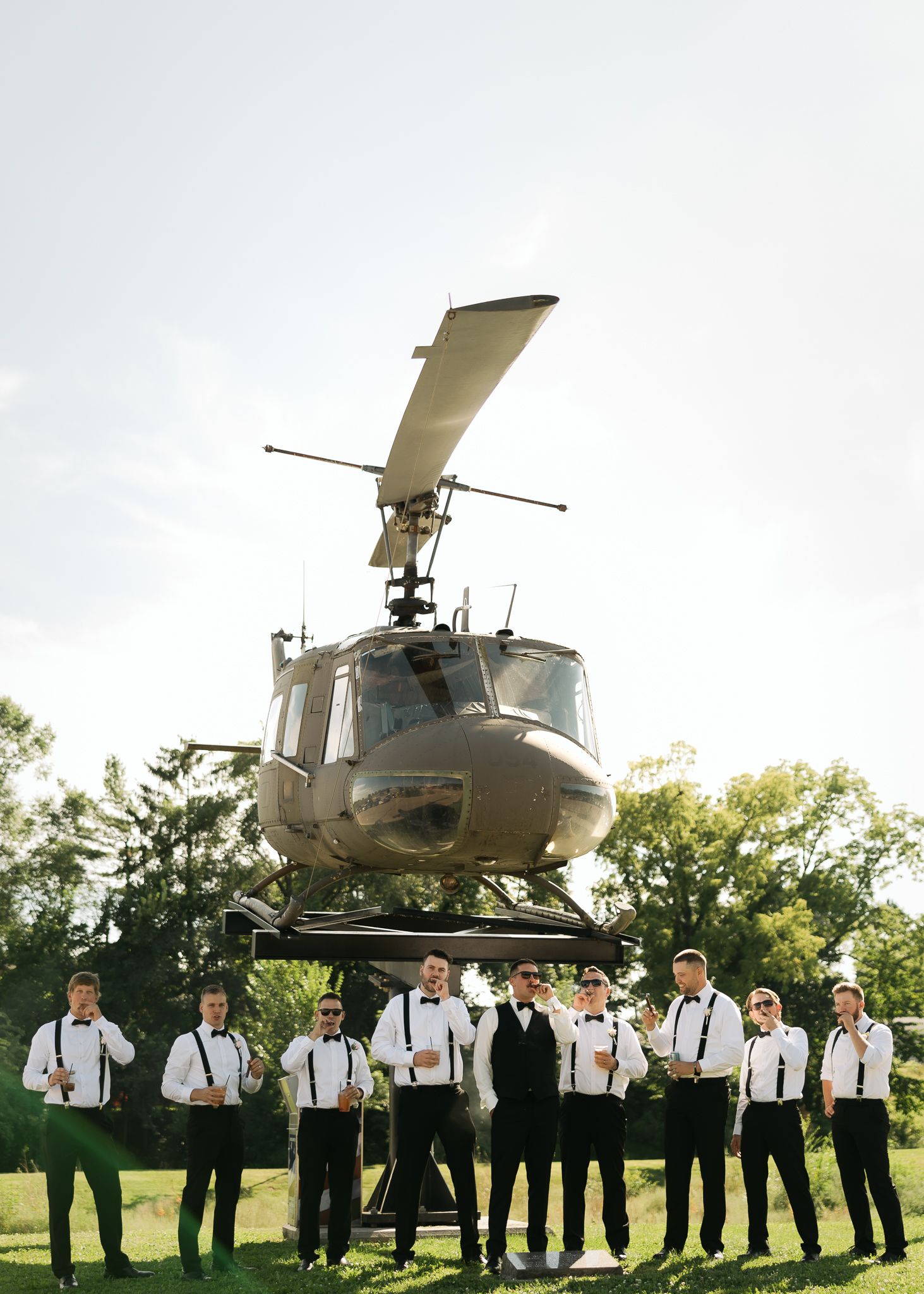 Wedding party poses in front of a military helicopter in an outdoor setting.
