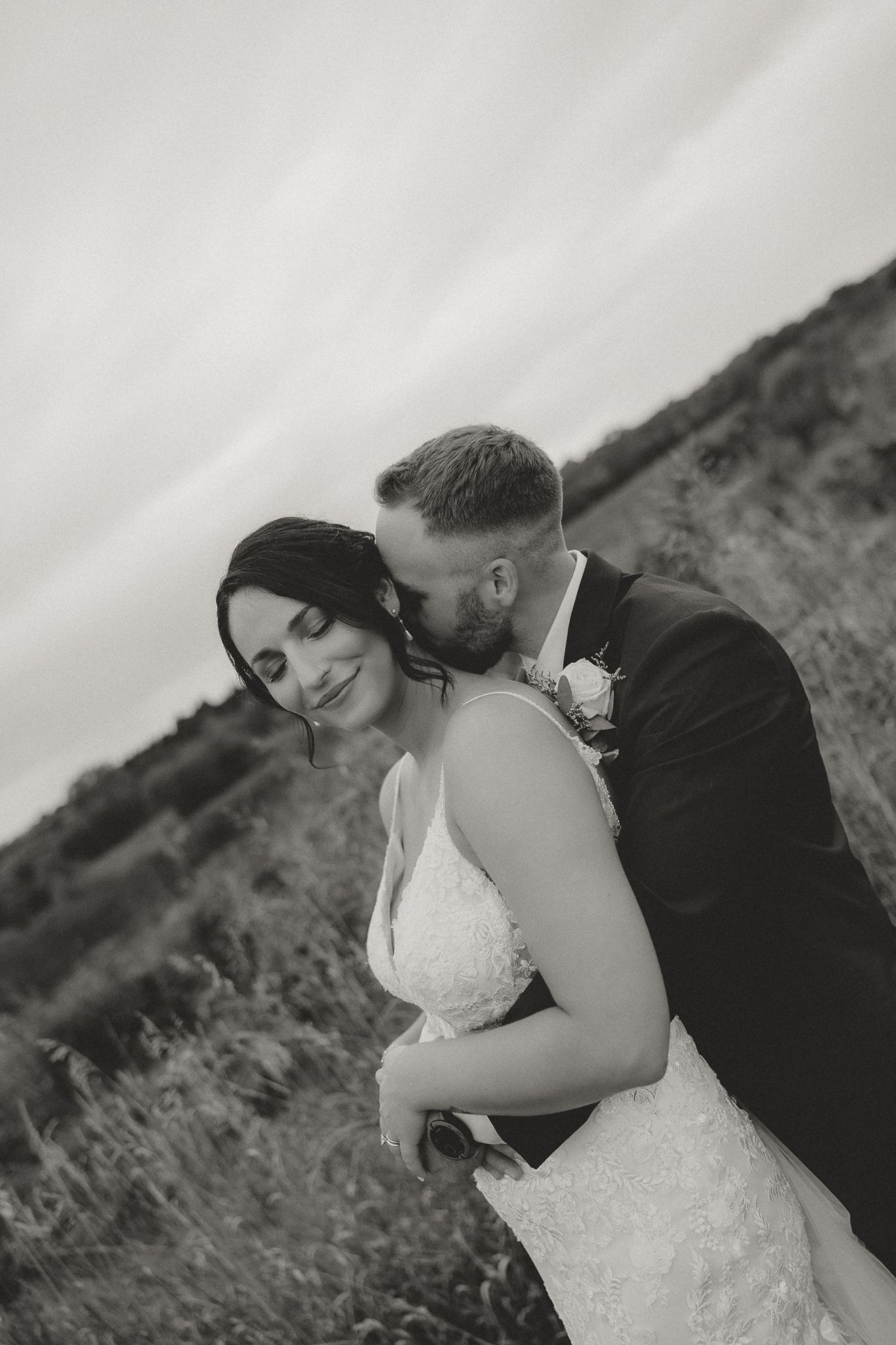 Black and white portrait of newlyweds sharing an intimate moment in a rustic outdoor setting.