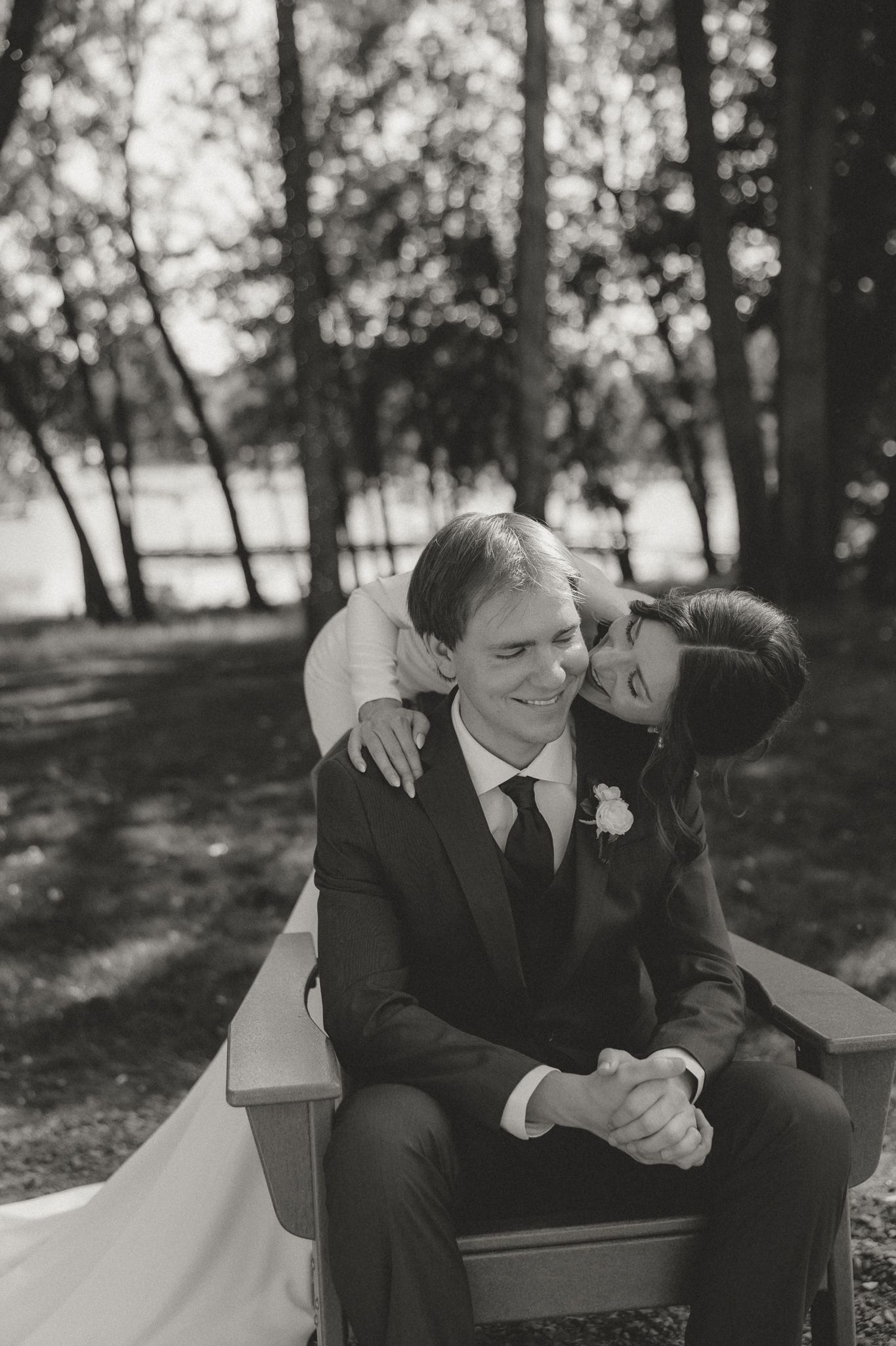 A black and white photo captures a tender wedding moment on a bench outdoors.