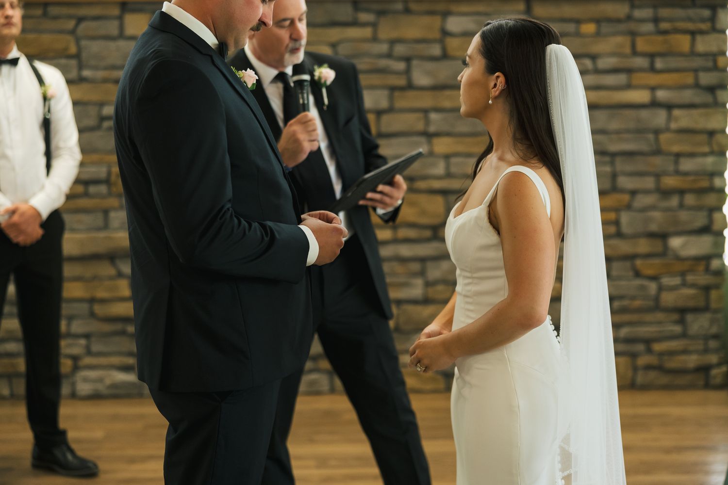 Wedding ceremony taking place against a rustic stone wall backdrop.