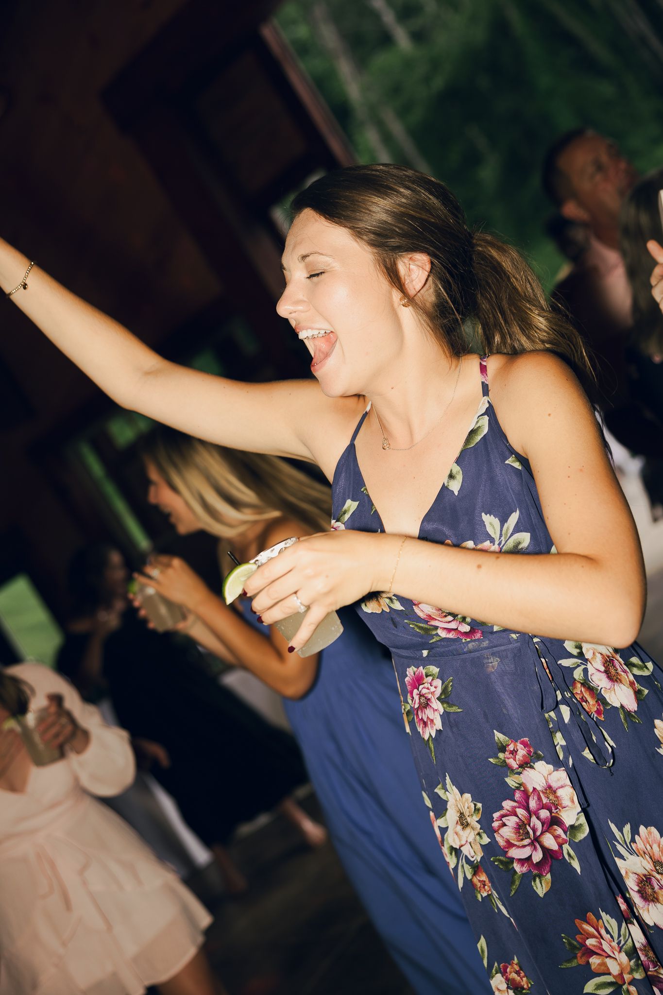 Woman in a navy floral dress dancing enthusiastically at a party under dim lighting.