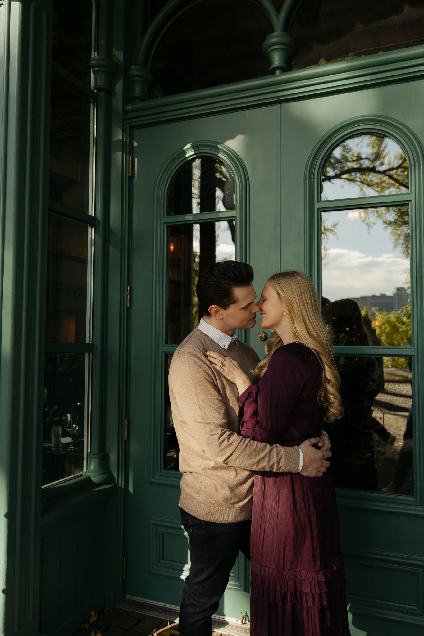 A couple embracing near large windows with natural light streaming in.