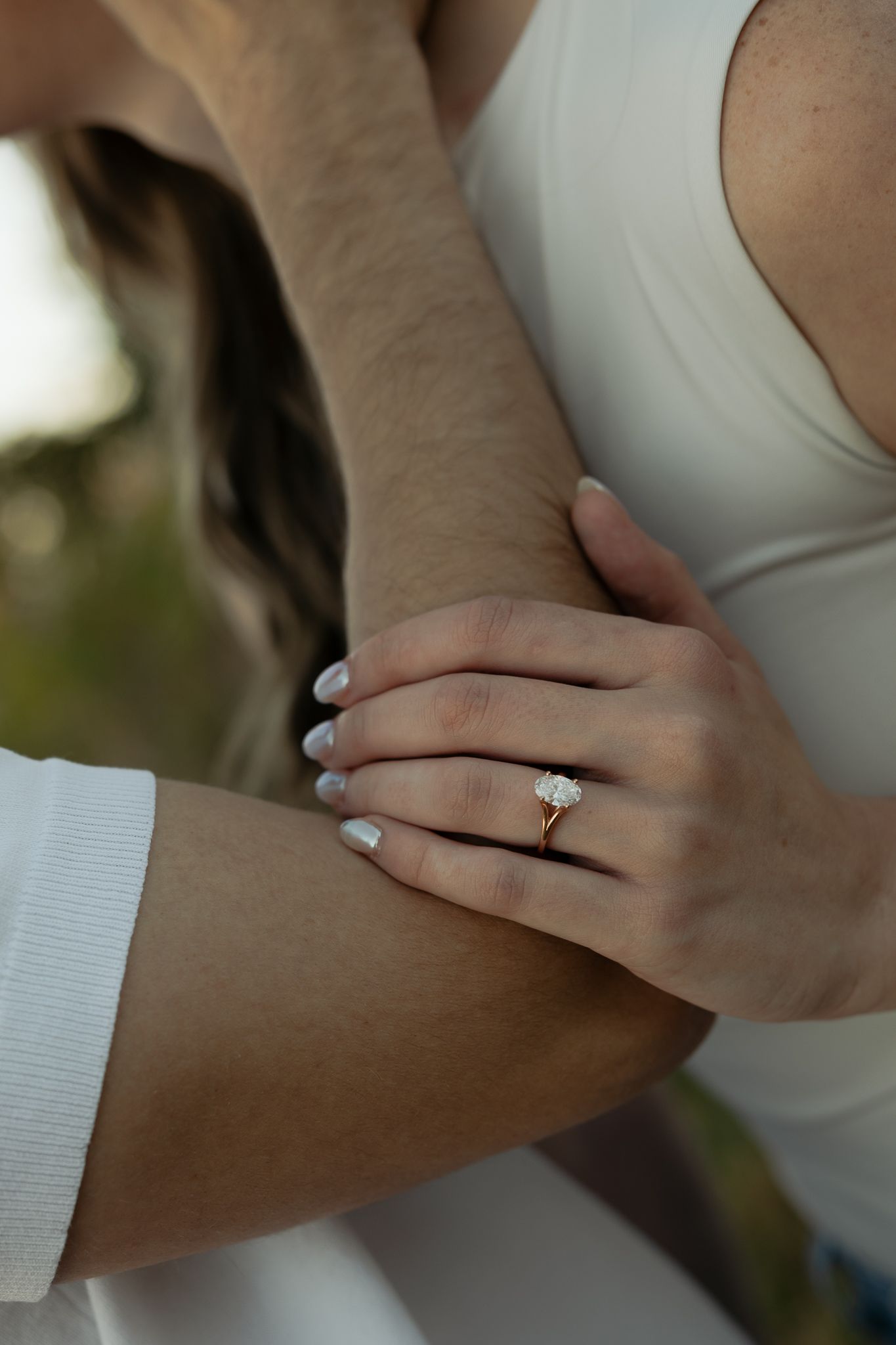 Close-up shot of hands showing off an engagement ring against a white top.