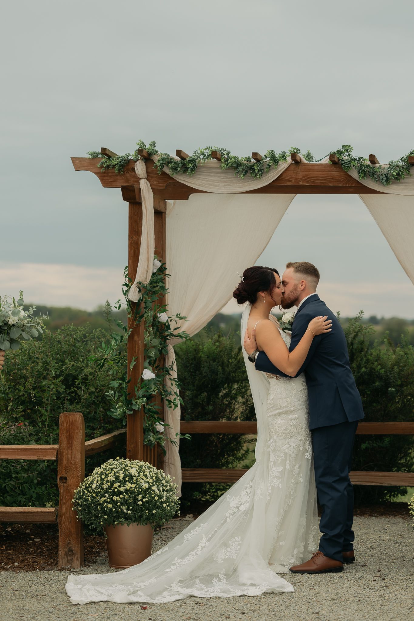 Romantic wedding ceremony moments under decorated wooden pergola with flowing white fabric.