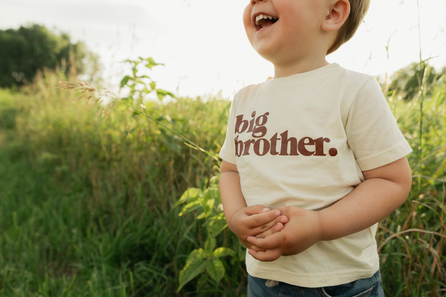 A laughing child plays outdoors wearing a cream colored t-shirt.