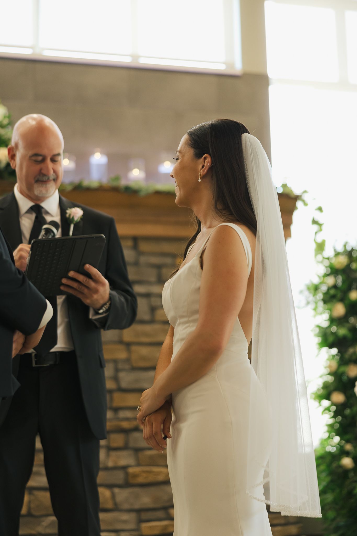 Wedding ceremony in progress inside venue with stone wall backdrop and natural lighting.