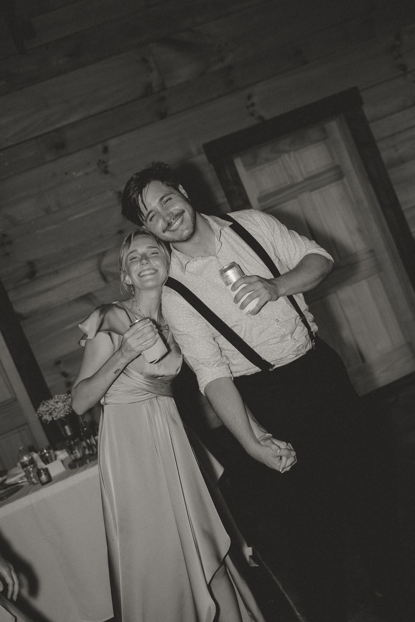Candid black and white photo of wedding guests dancing and laughing in a dimly lit venue.
