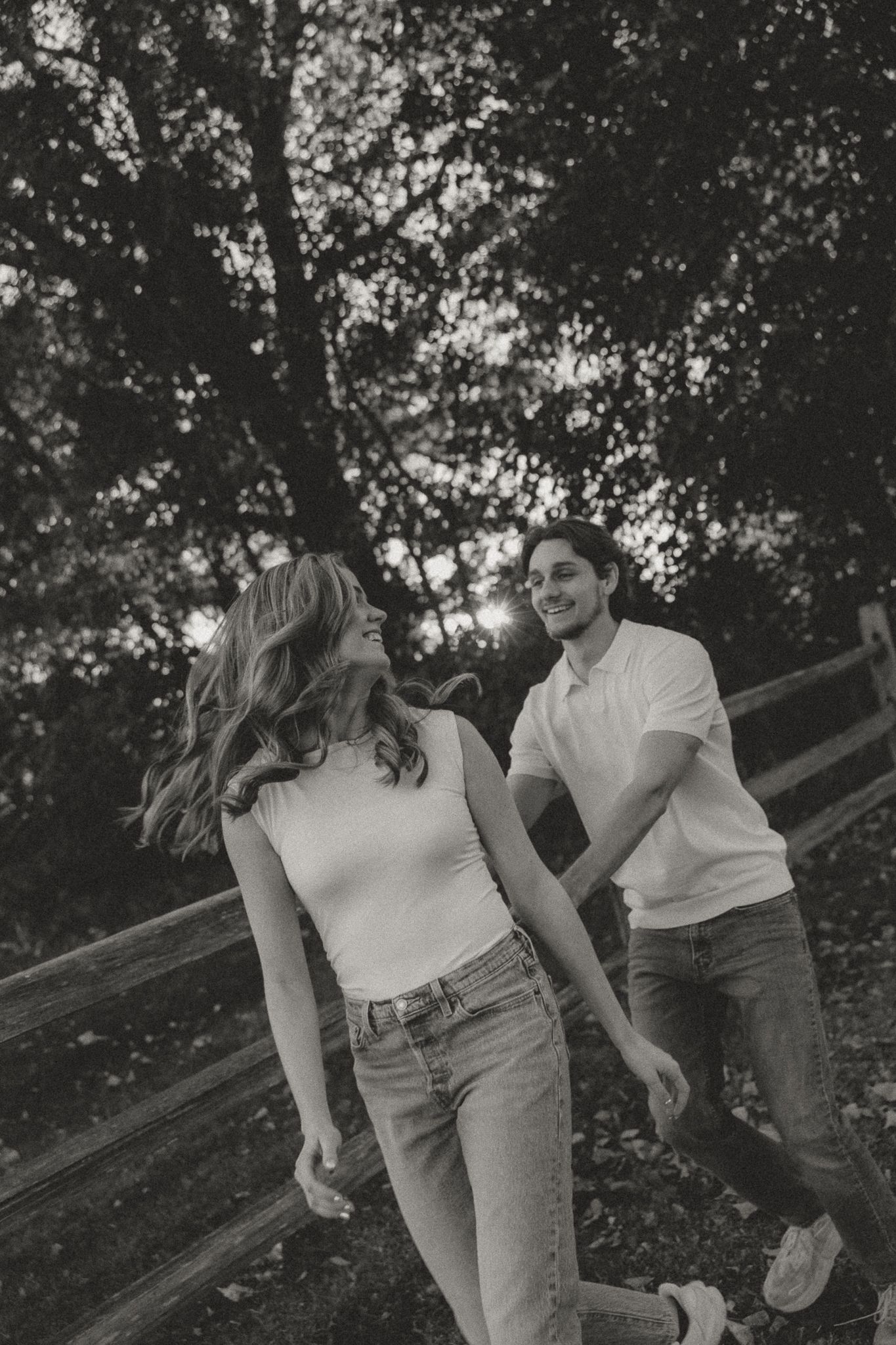 Romantic couple in casual outfits sharing intimate moments by a wooden fence in a natural outdoor setting.