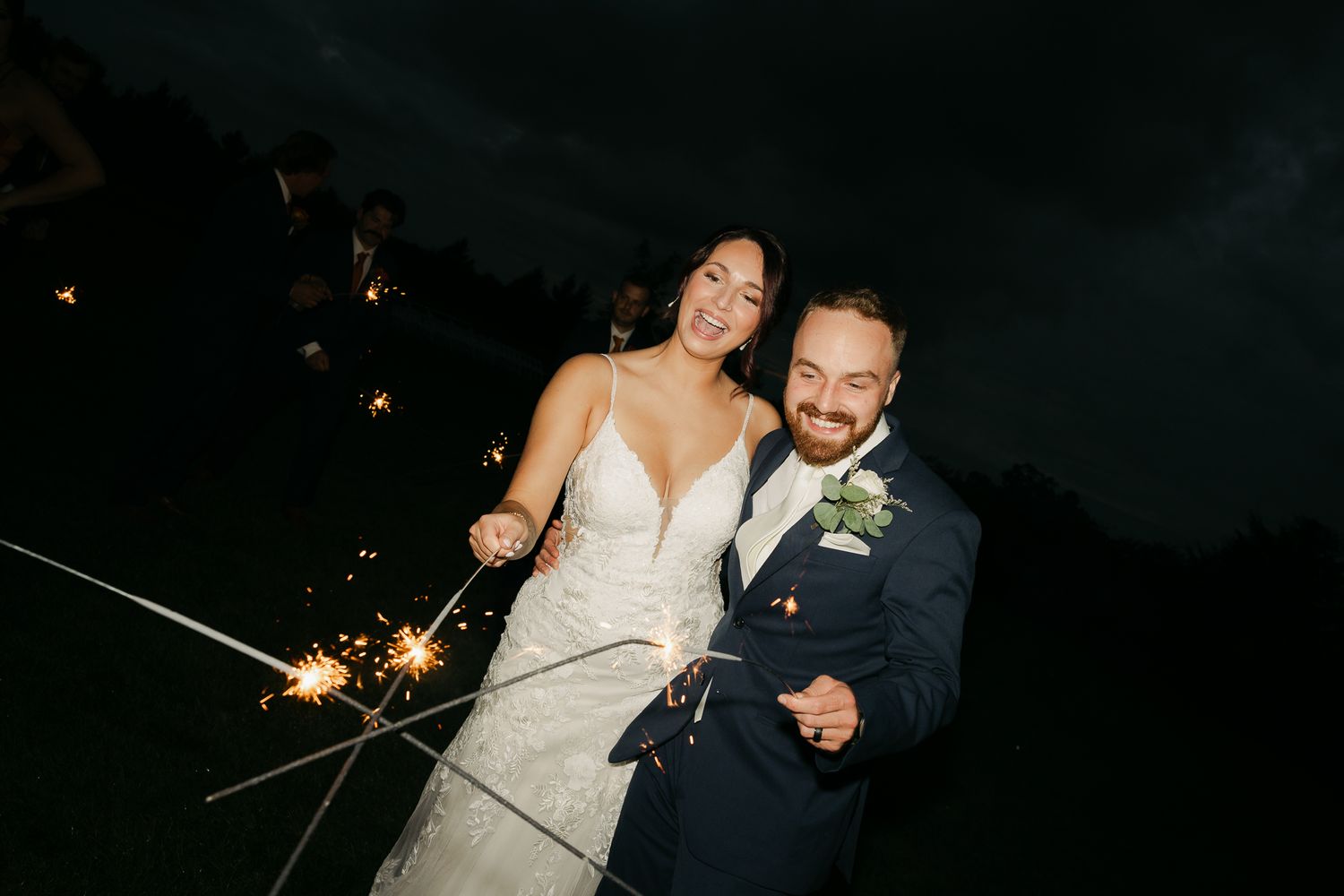 Couple in wedding attire holds sparklers during nighttime celebration.