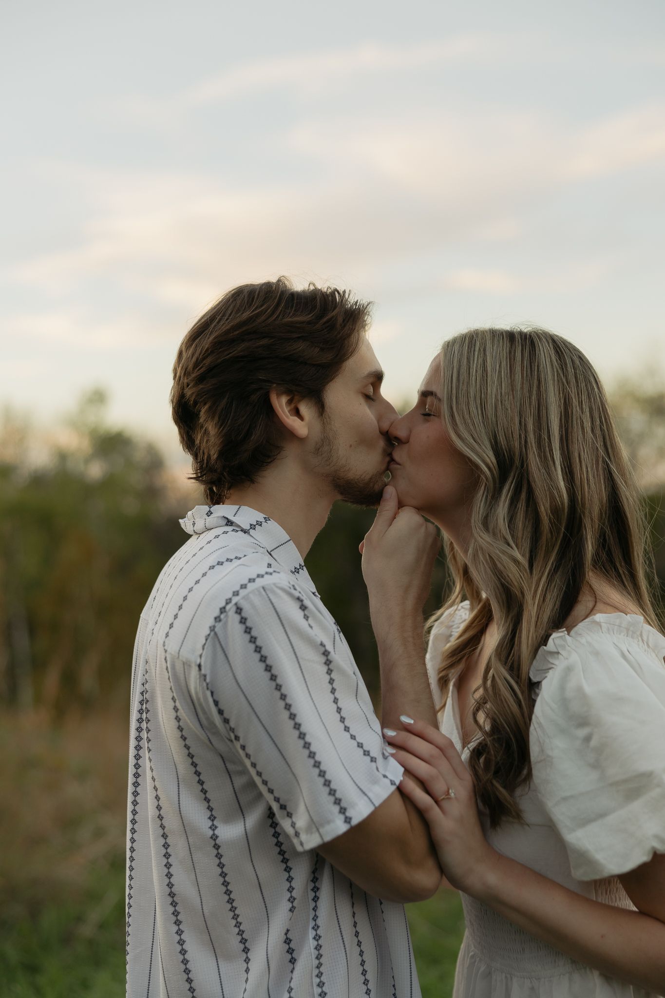 An intimate moment between a couple in white clothing against a sunset sky.