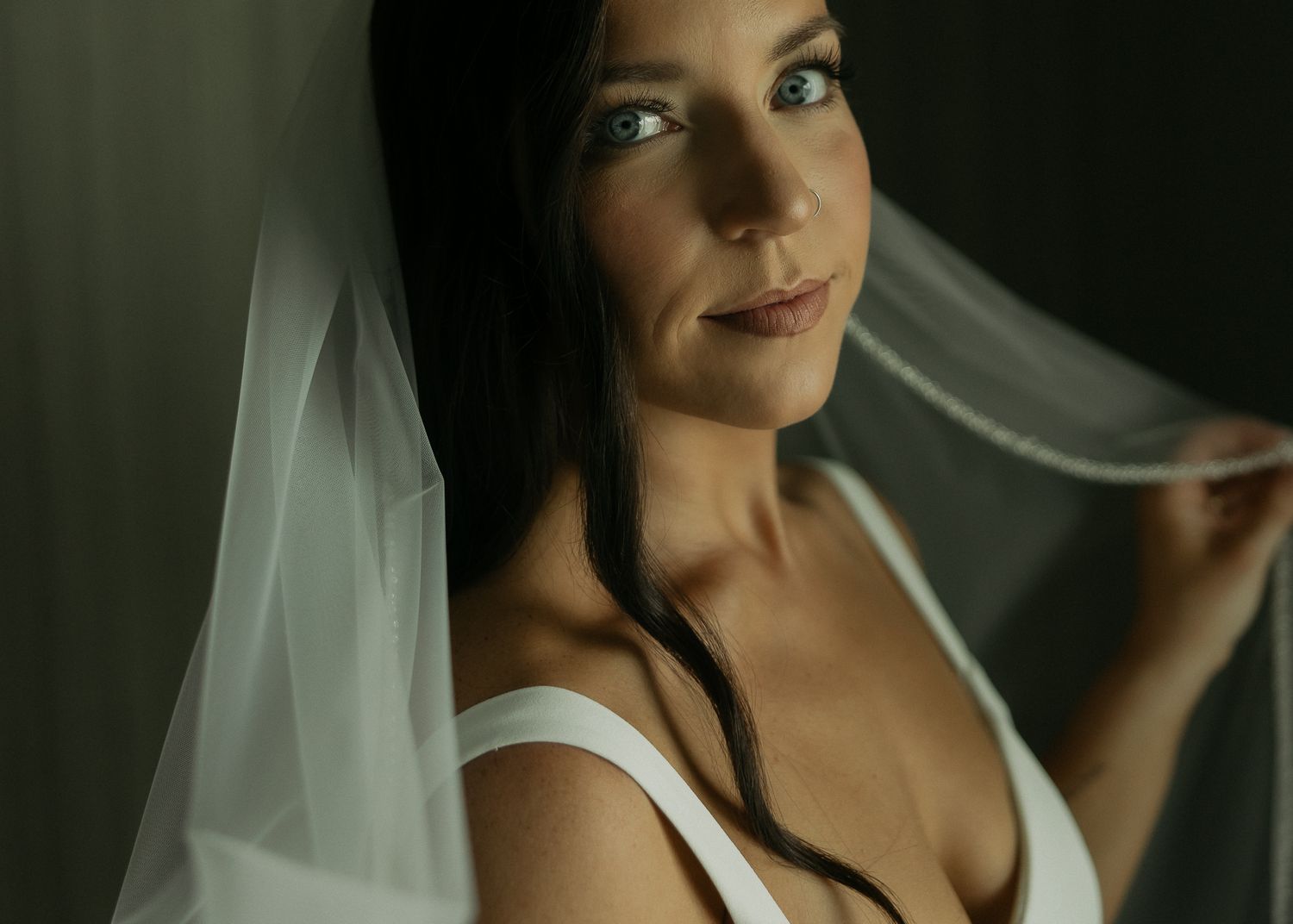 Close-up portrait of a bride in white dress with delicate veil against dark background.