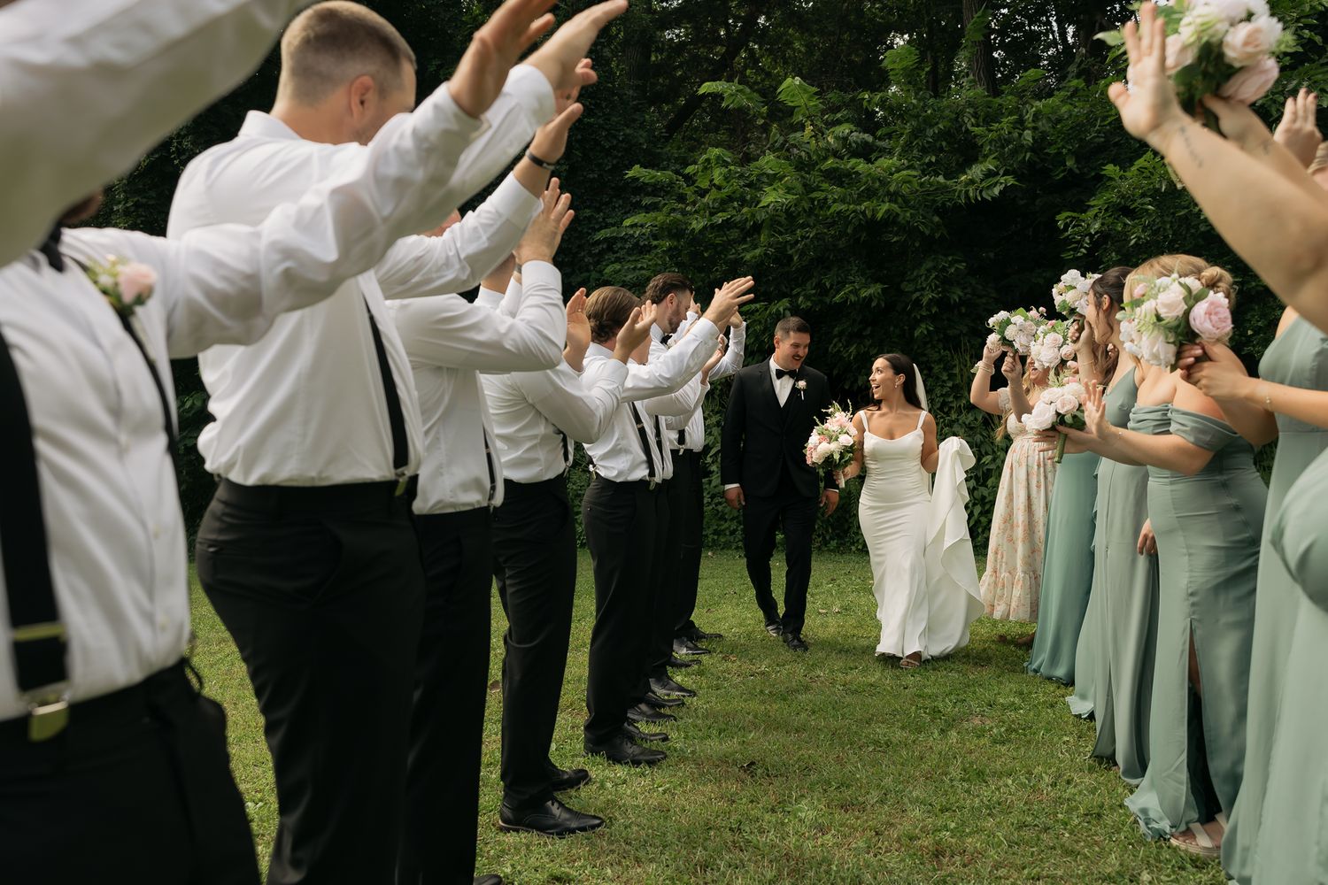 Wedding party forms a tunnel with raised arms as newlyweds walk through on their special day.