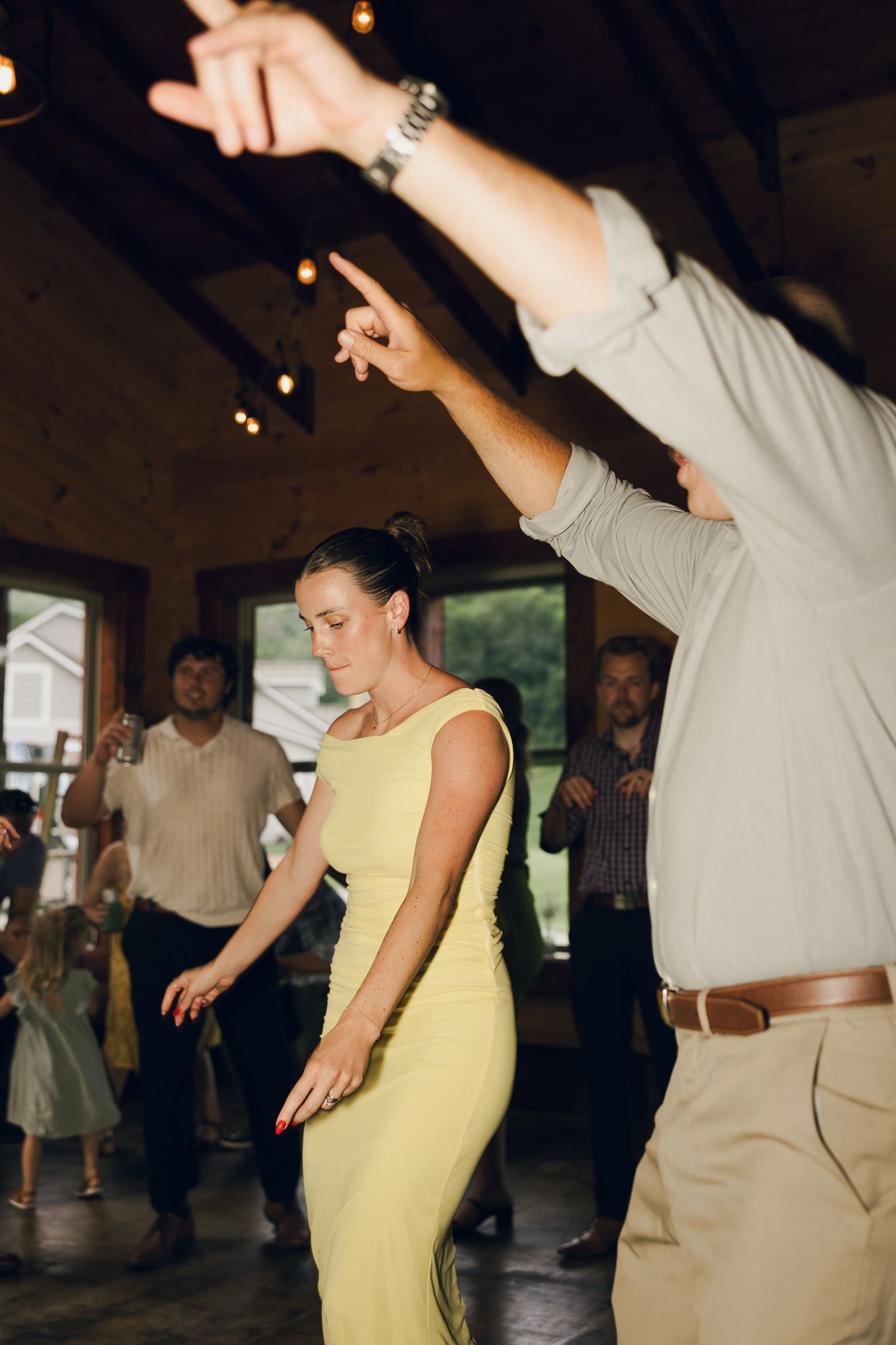 Wedding guests dancing with raised arms in a rustic venue with string lights.