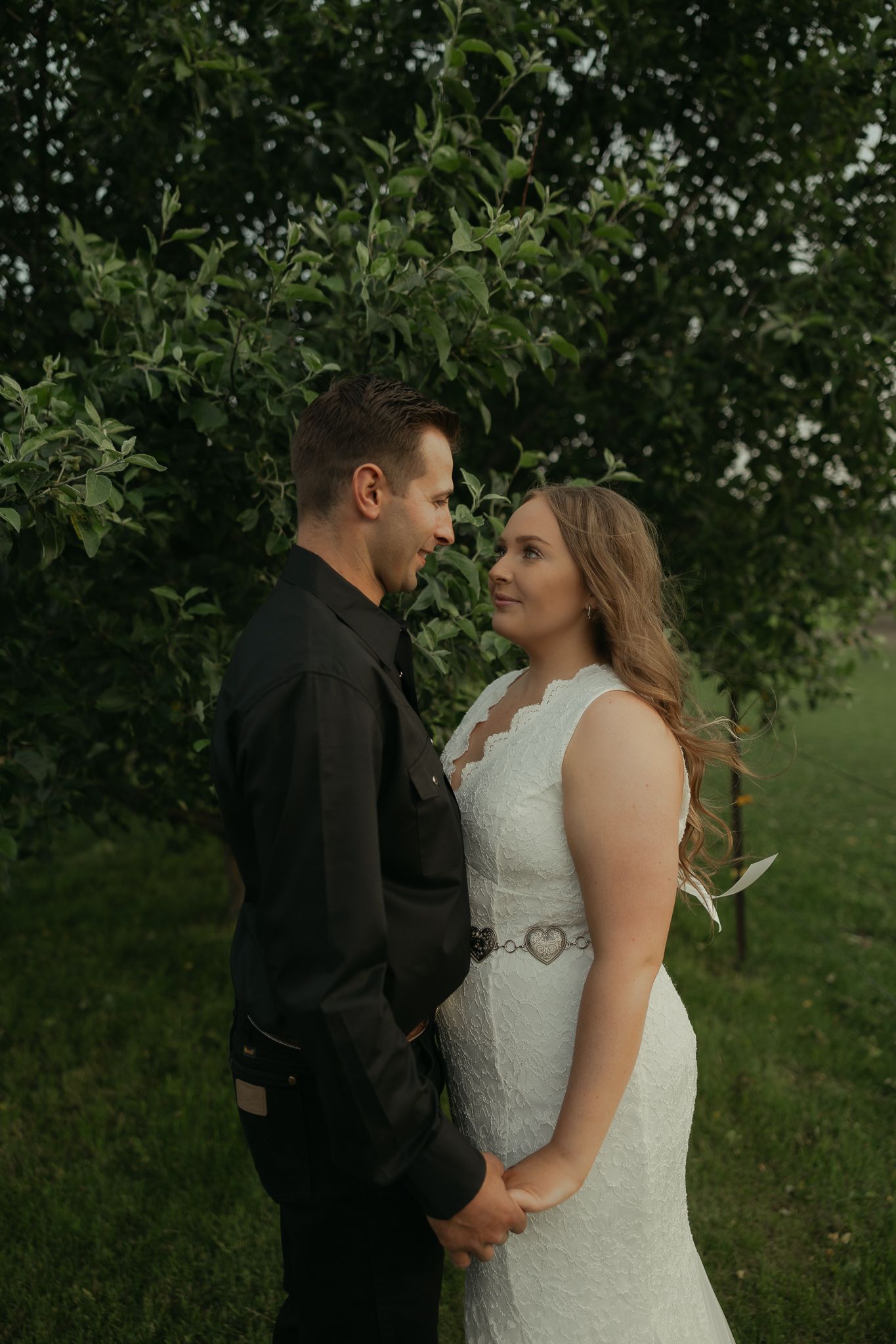 A romantic couple embraces in front of lush greenery during an outdoor photoshoot.