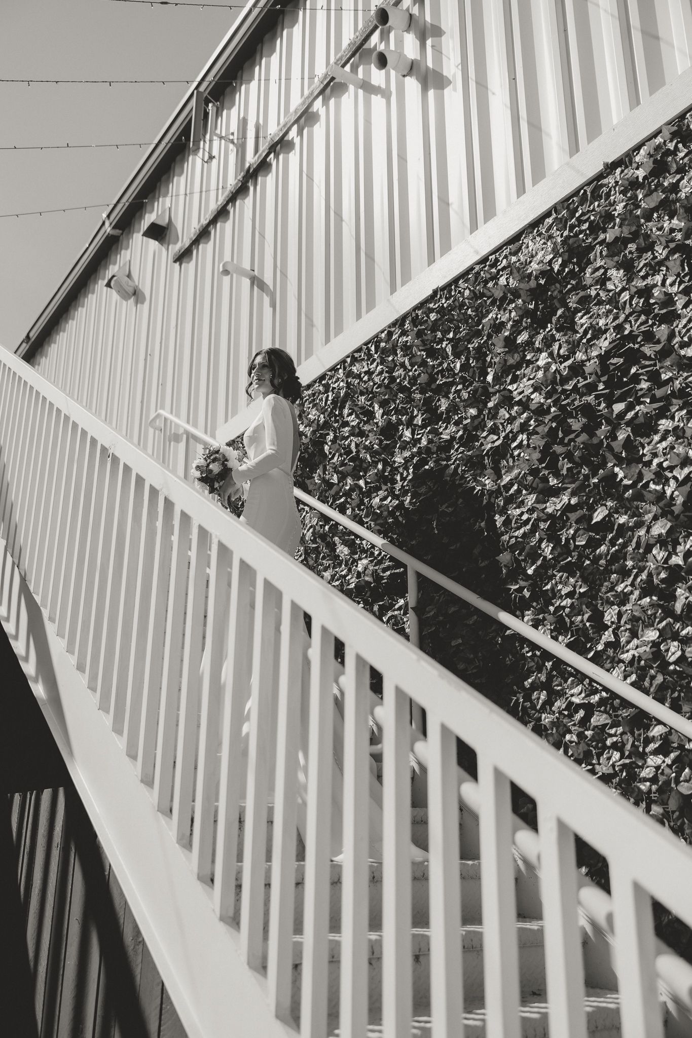 Black and white photo of person ascending white staircase with ivy-covered wall.