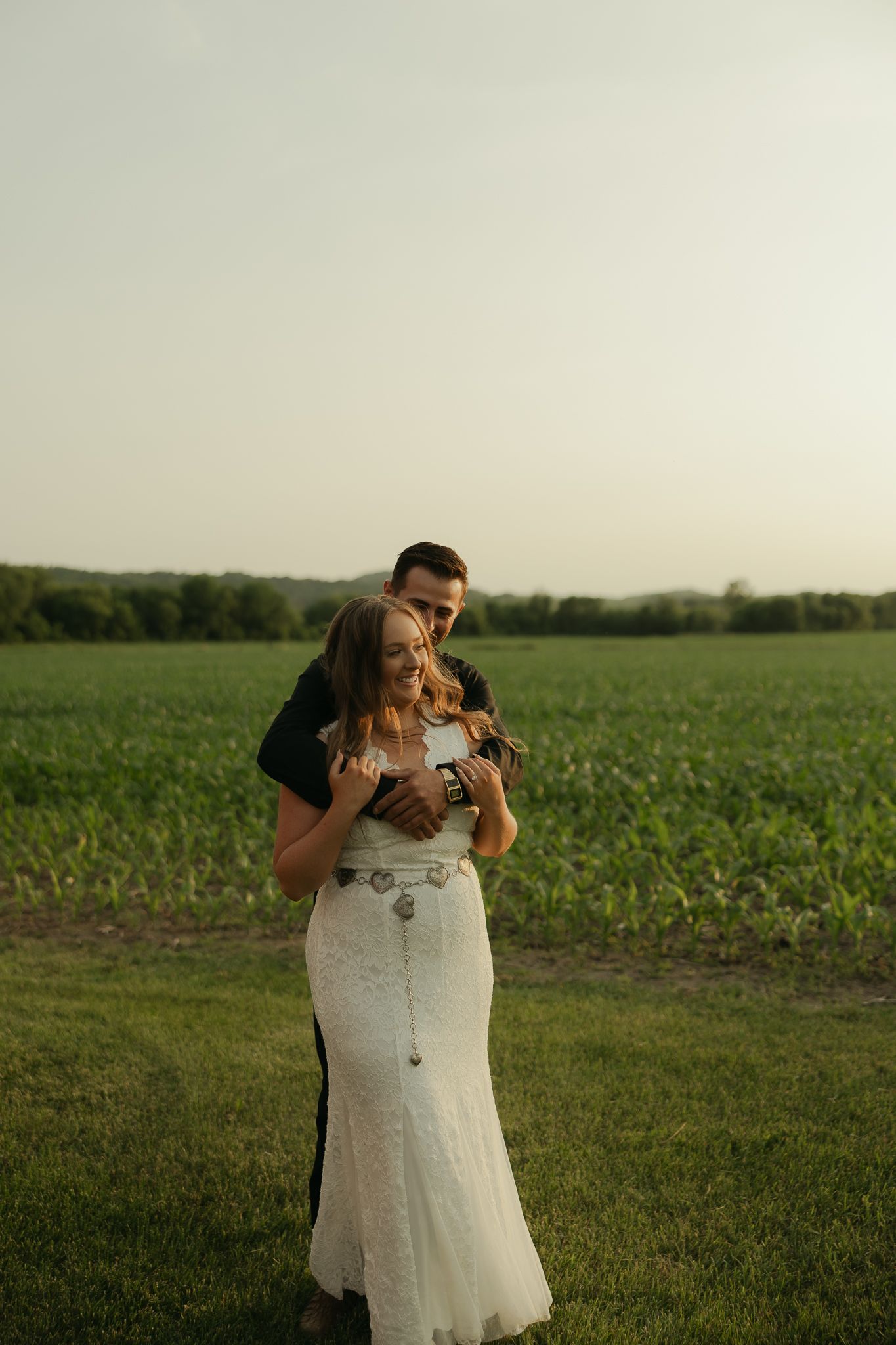 A couple shares an intimate moment at the edge of a cornfield during sunset.