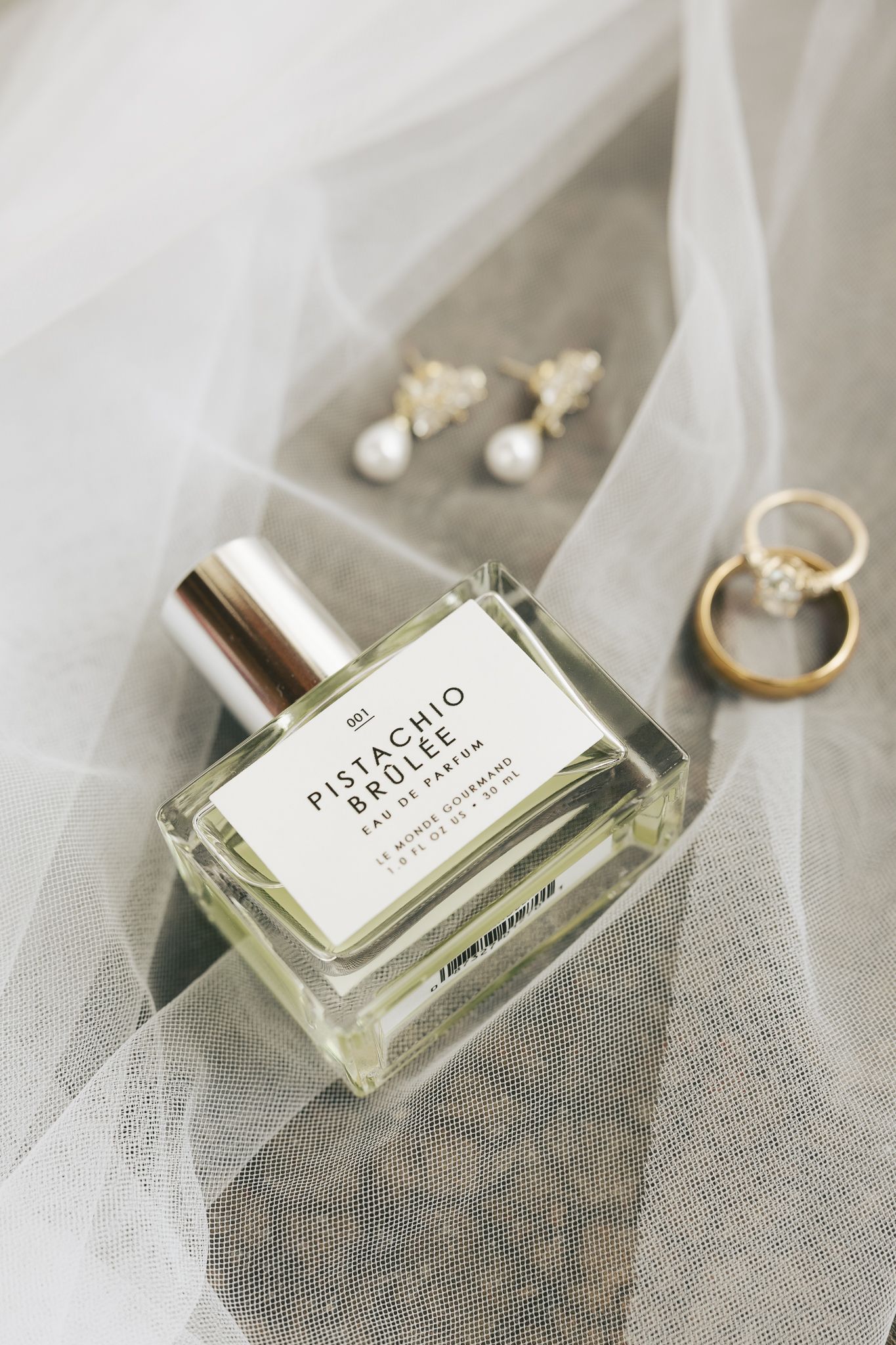 Elegant perfume bottle and wedding accessories arranged on delicate white tulle.