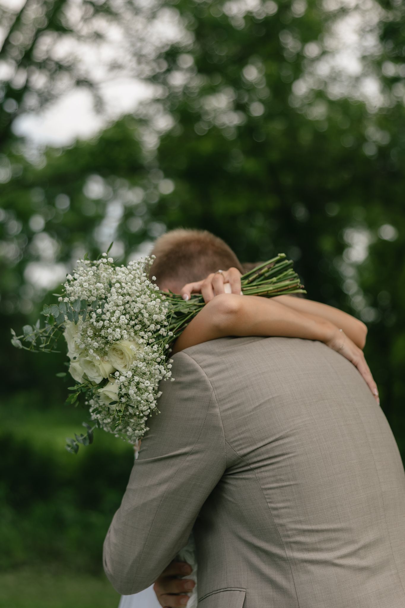 A close embrace between newlyweds with a white baby's breath bouquet visible.