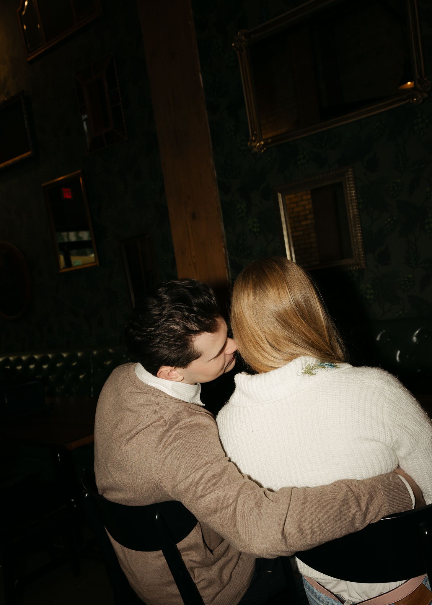 A couple sharing an intimate moment on a dark leather couch in a dimly lit room.