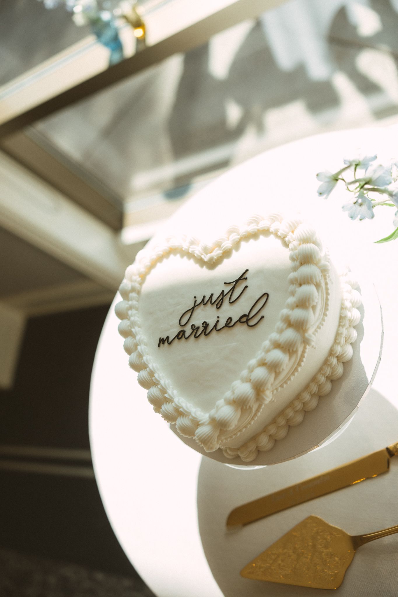 Heart-shaped white wedding cake with pearl details and gold 'just married' topper on a white stand.