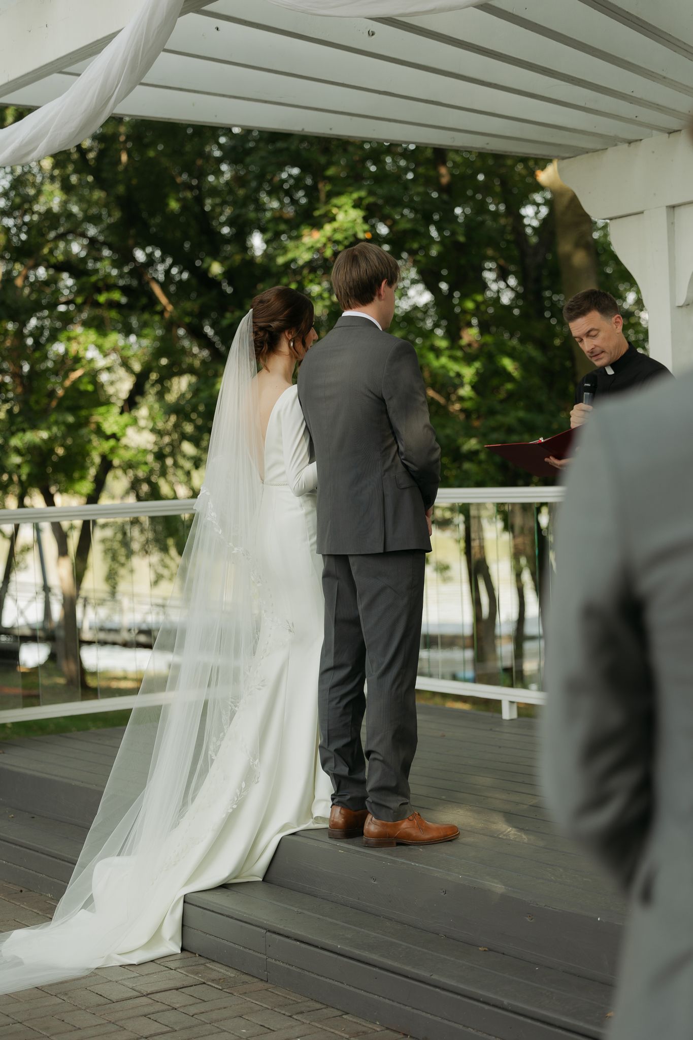 Wedding couple sharing intimate moment under white pergola during outdoor ceremony.