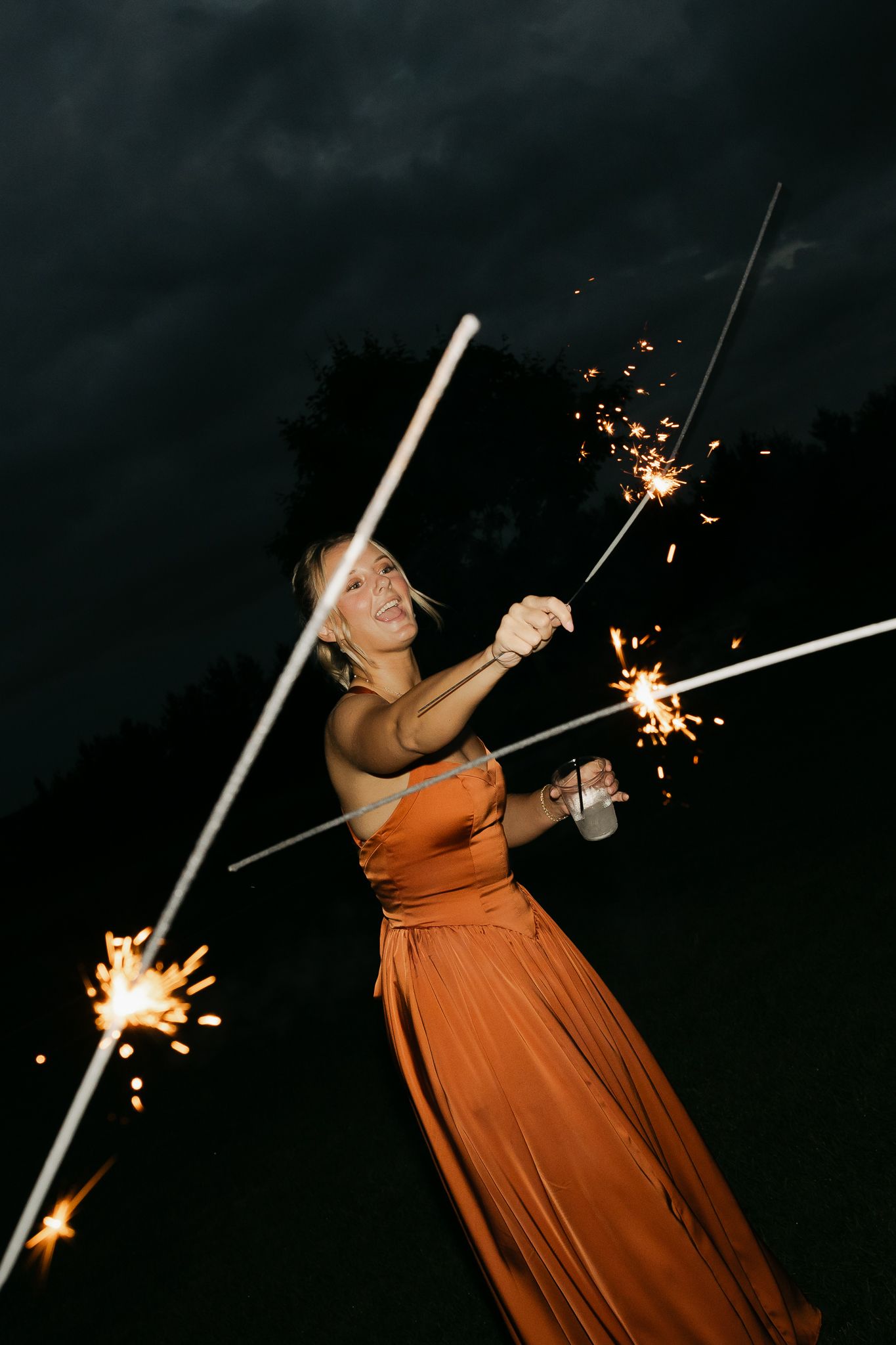 Woman in an orange dress twirls with sparklers creating light trails in the darkness.