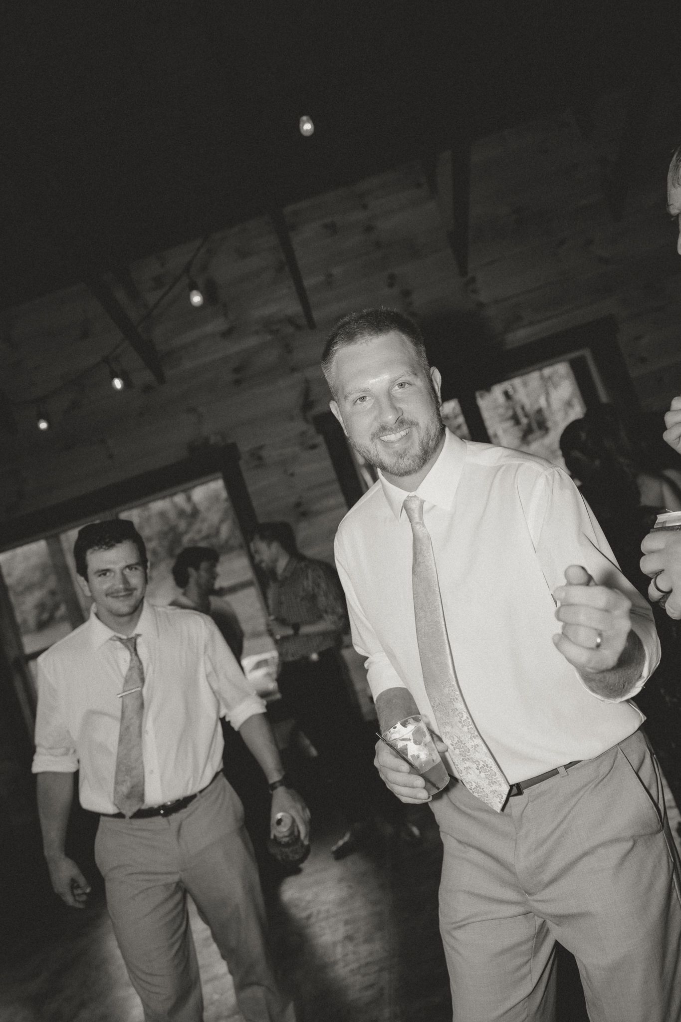Wedding guests in white shirts and suspenders dance energetically at a reception.