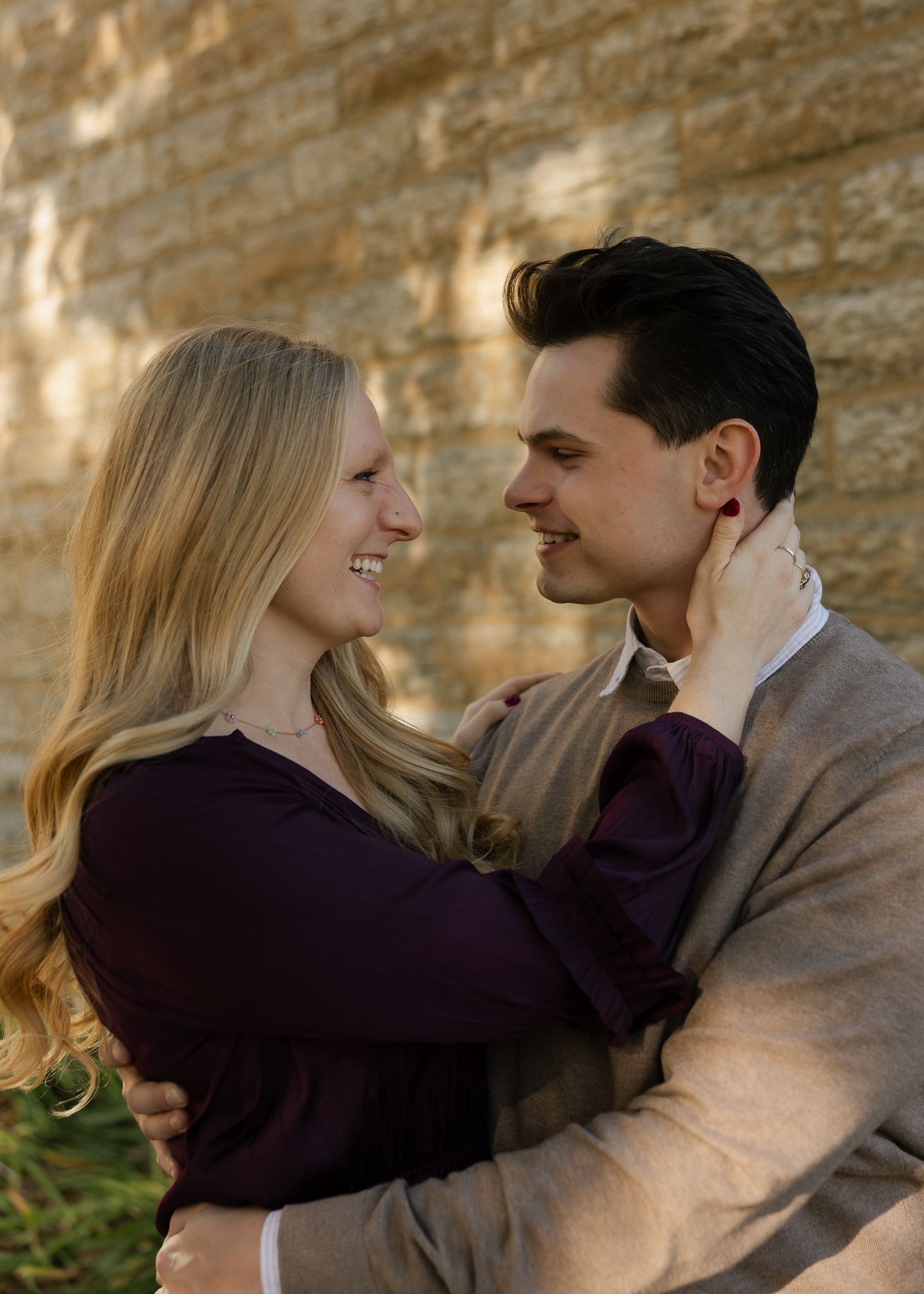 Couple embracing against a stone wall backdrop in warm autumn lighting.