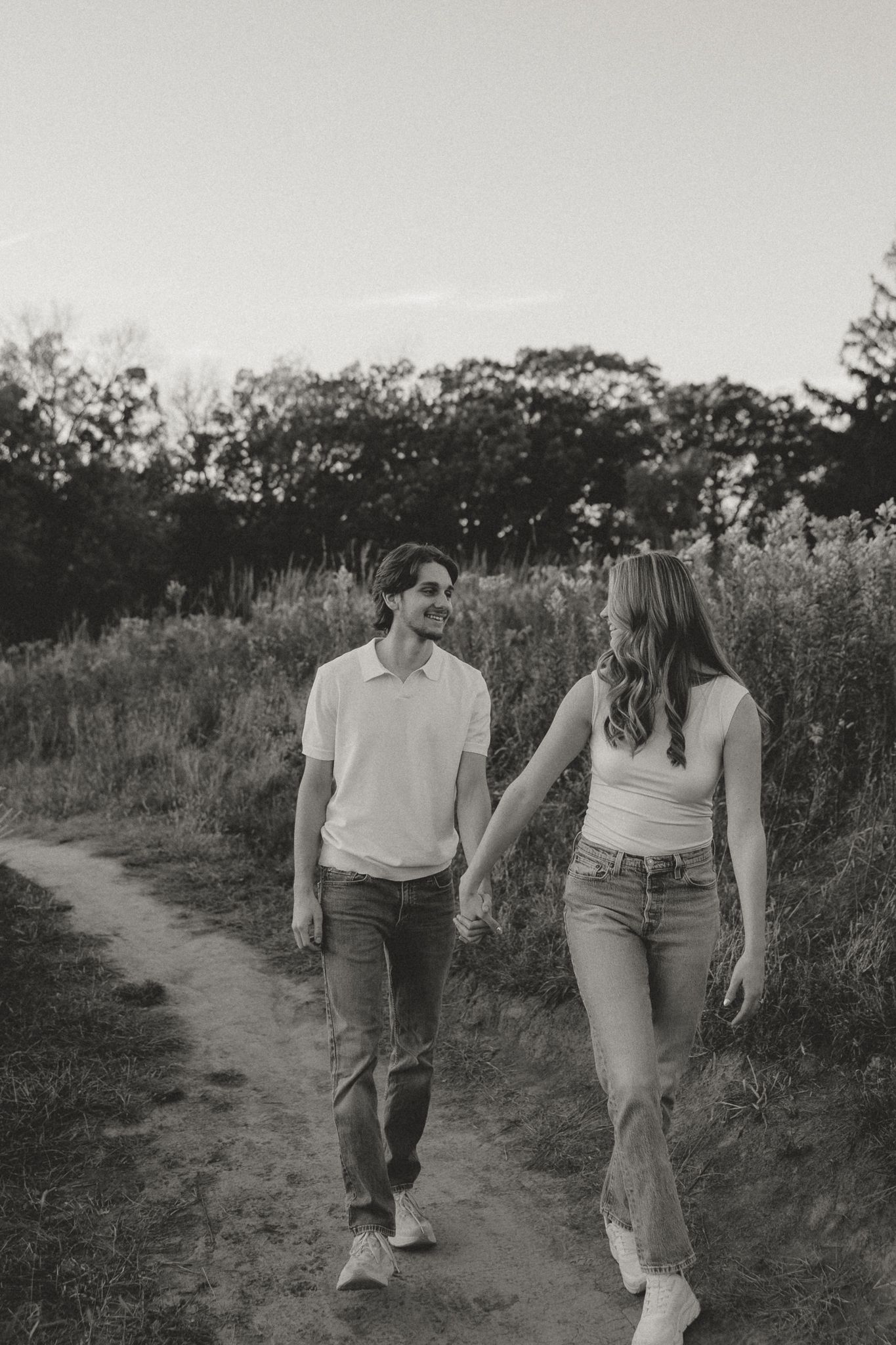 Black and white photo of a couple walking hand in hand along a nature trail.