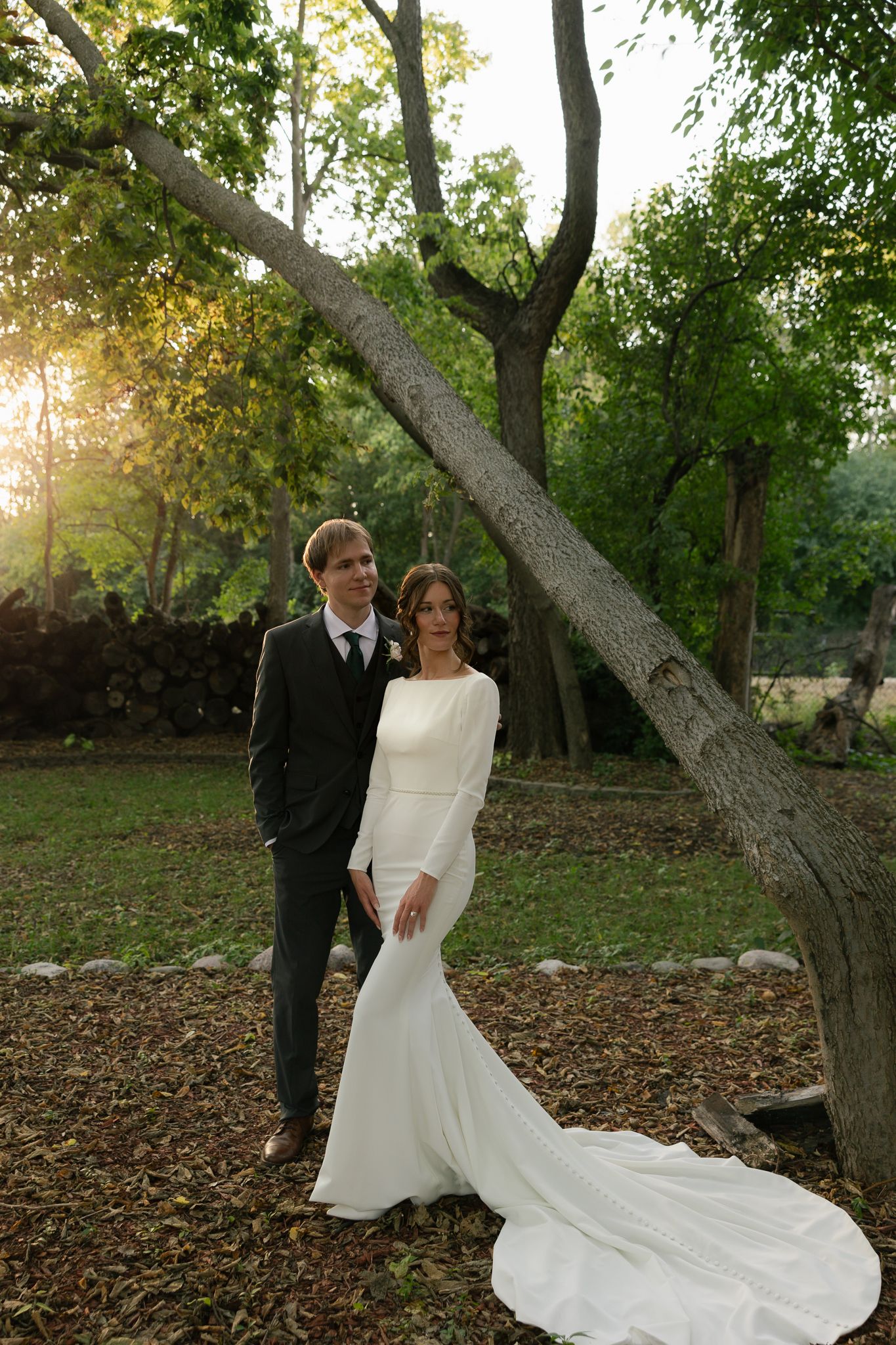 A couple poses in a wooded setting with a flowing white wedding dress train.