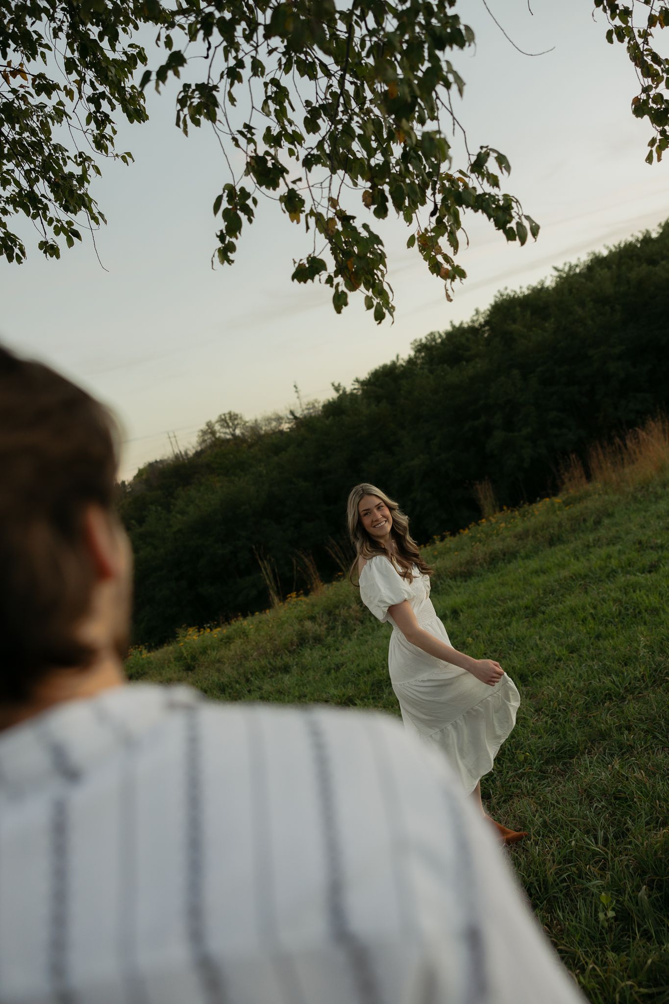 A woman in a white dress twirls in a grassy field at sunset.