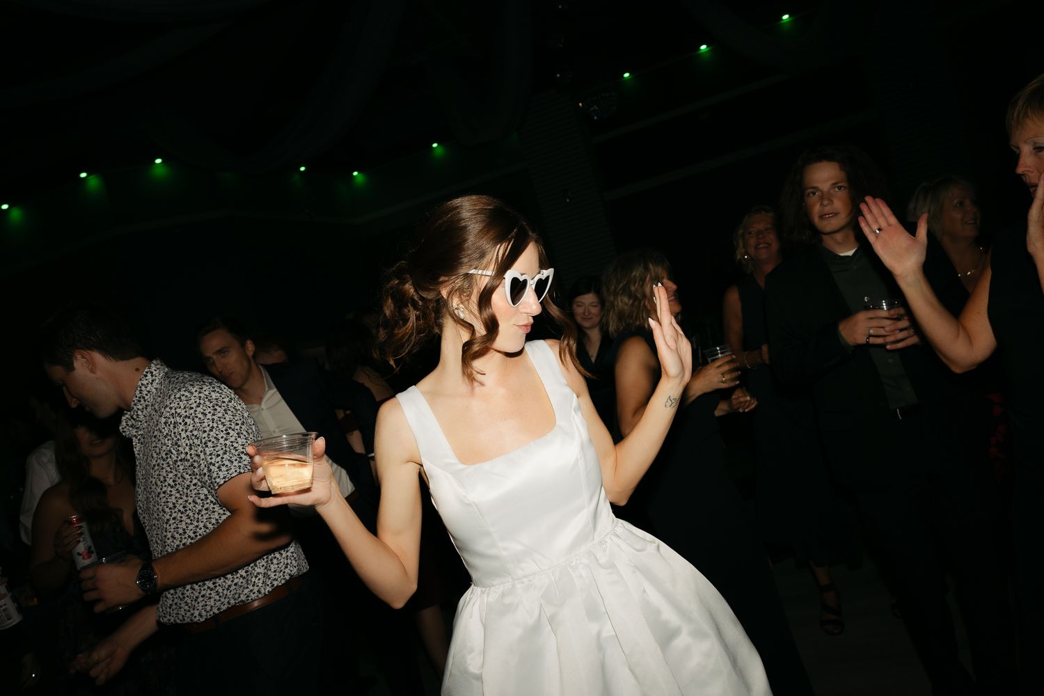 Wedding guests dancing and celebrating at a dark reception venue with dramatic lighting.