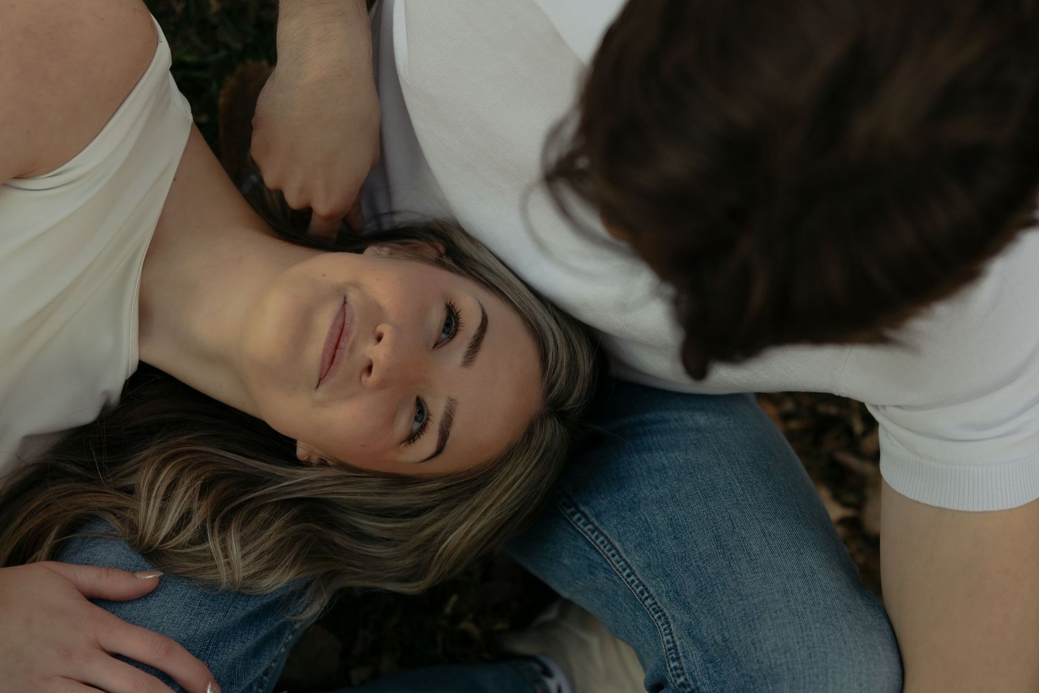 Two women sharing a tender moment, one lying down smiling with eyes closed while another leans over her gently.