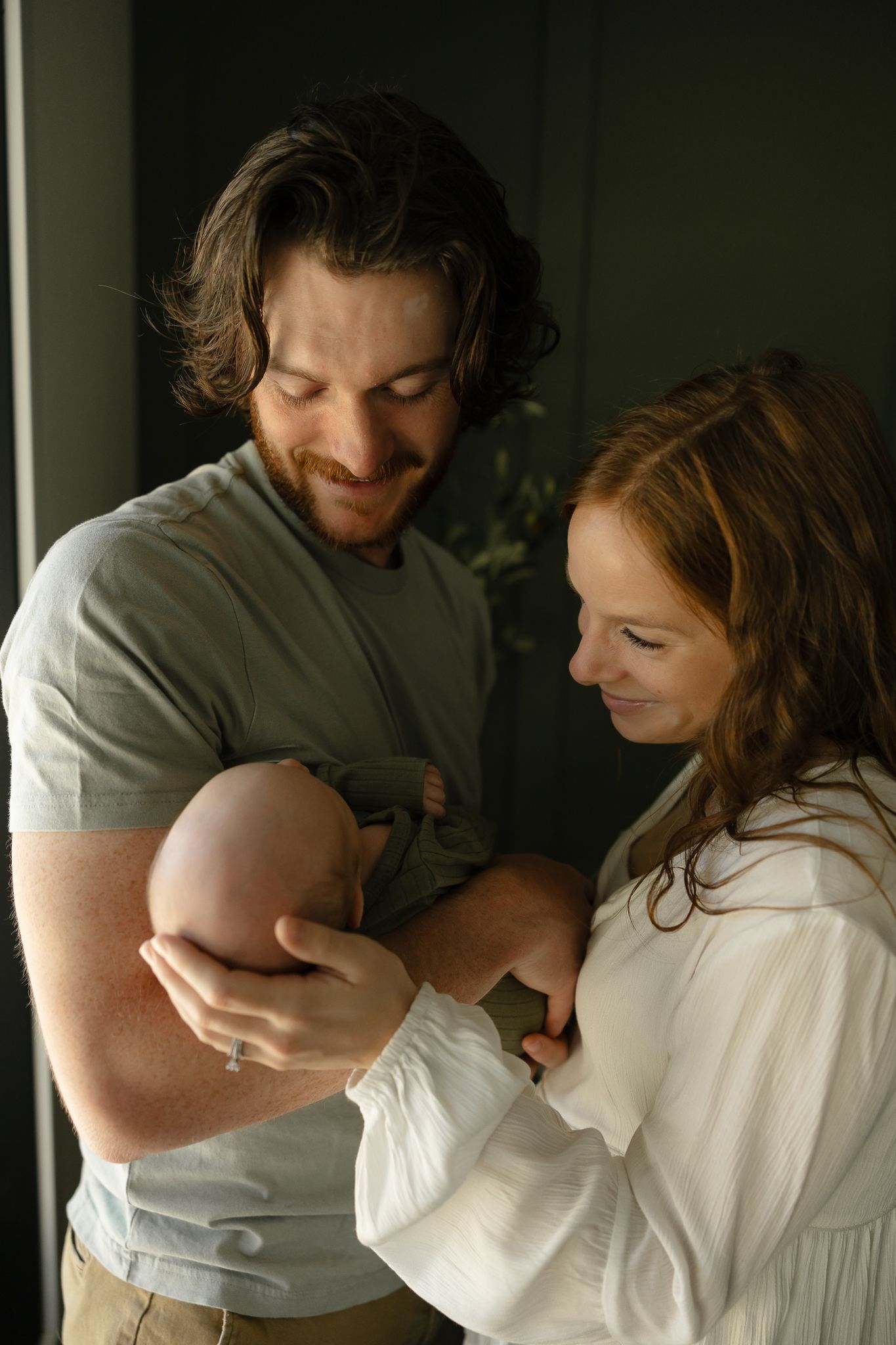 Intimate couple embraces in casual clothing against dark background in home setting.