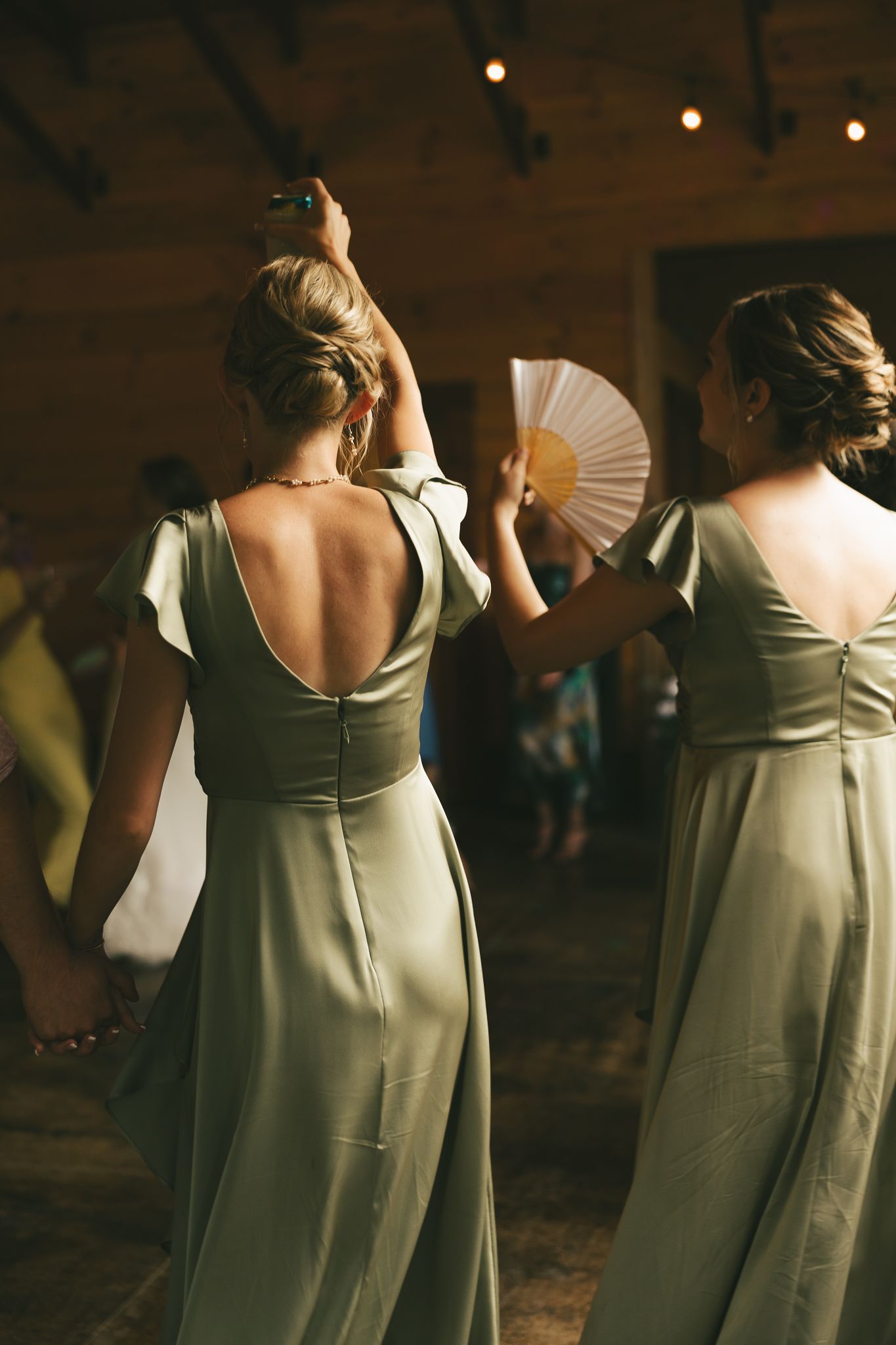 Bridesmaids in sage green dresses dancing at a wedding reception.