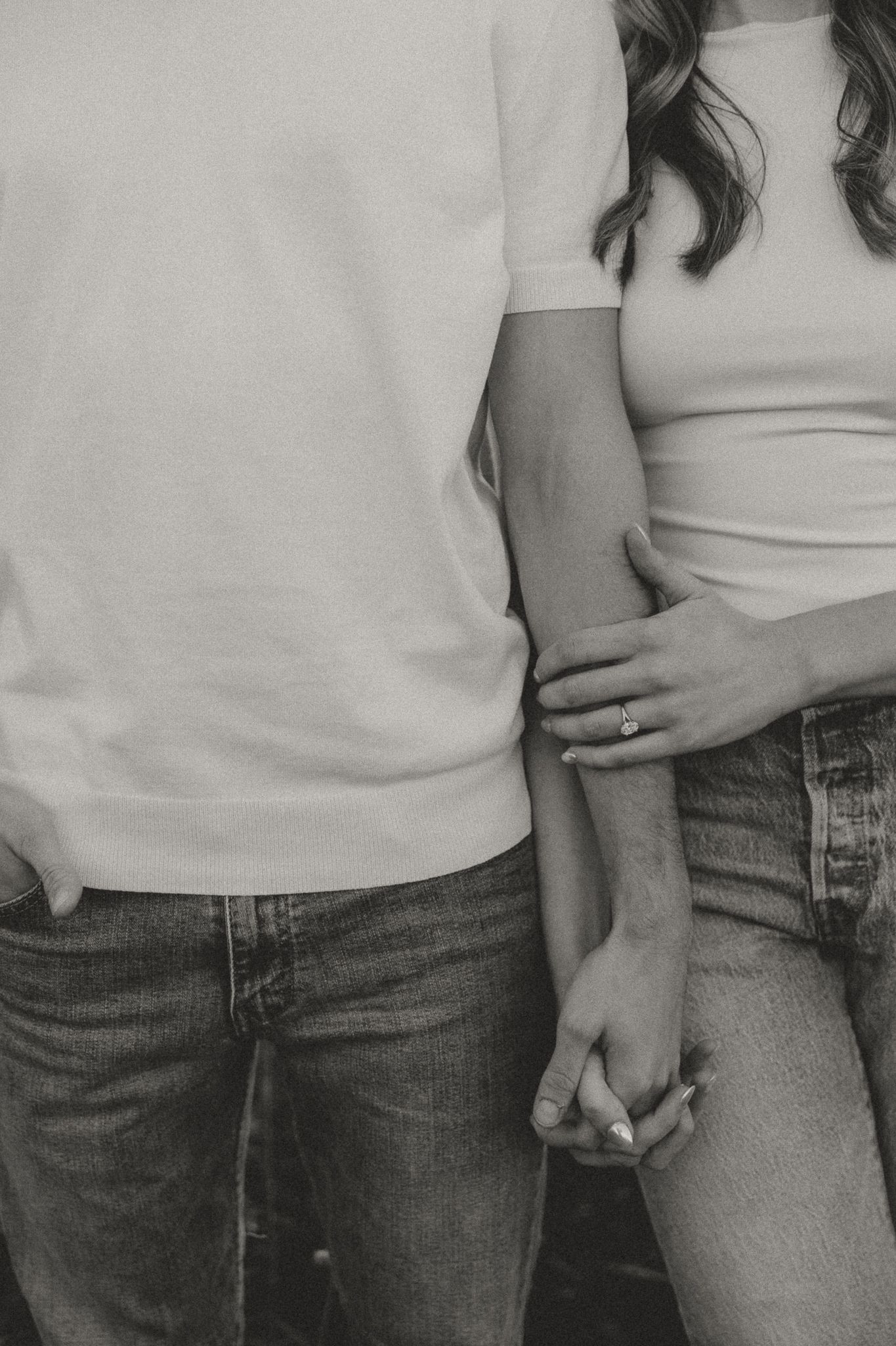 Close-up black and white shot of couple in casual wear holding hands.