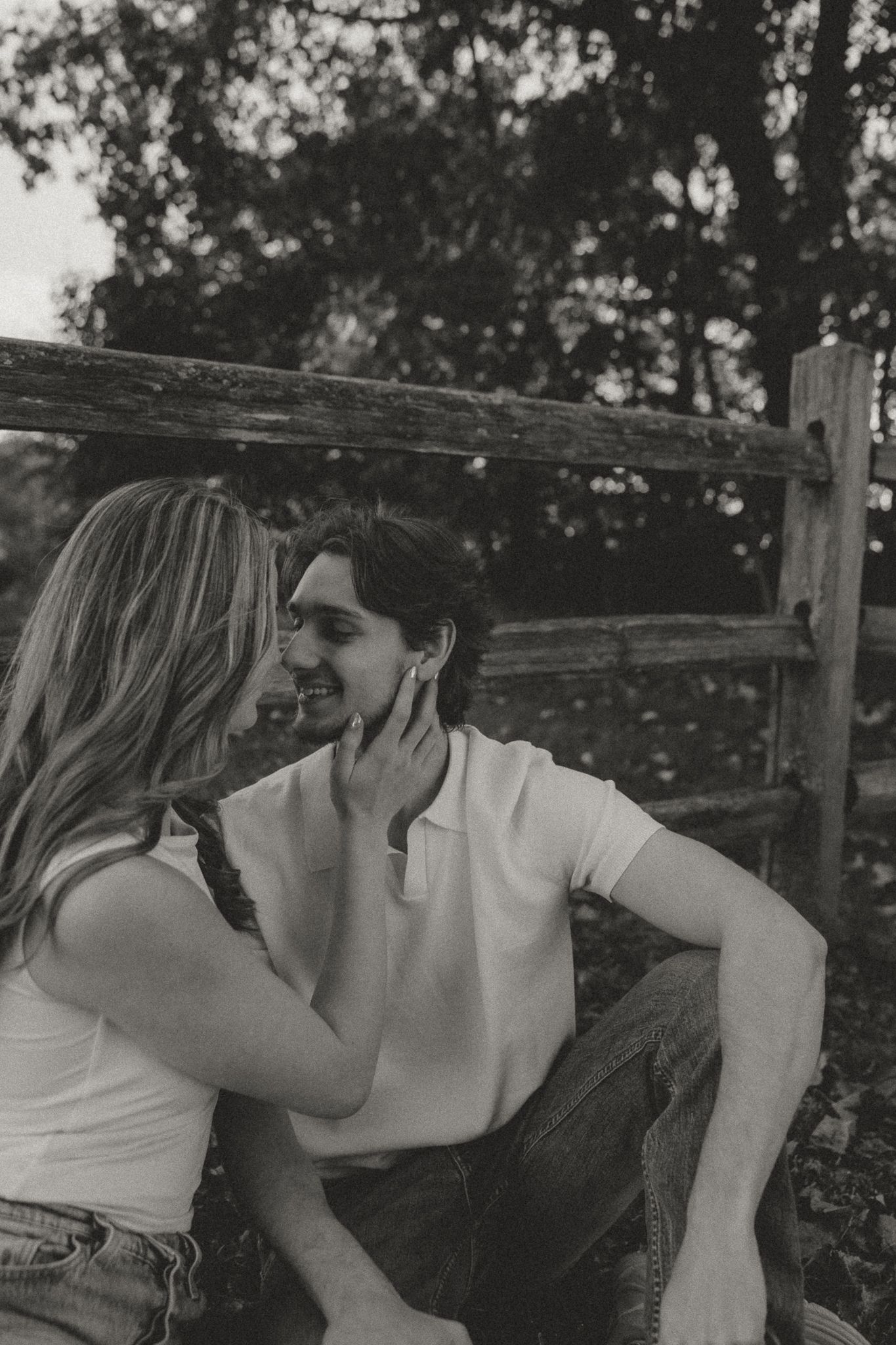 Romantic black and white portrait of couple sharing tender moments by wooden fence.