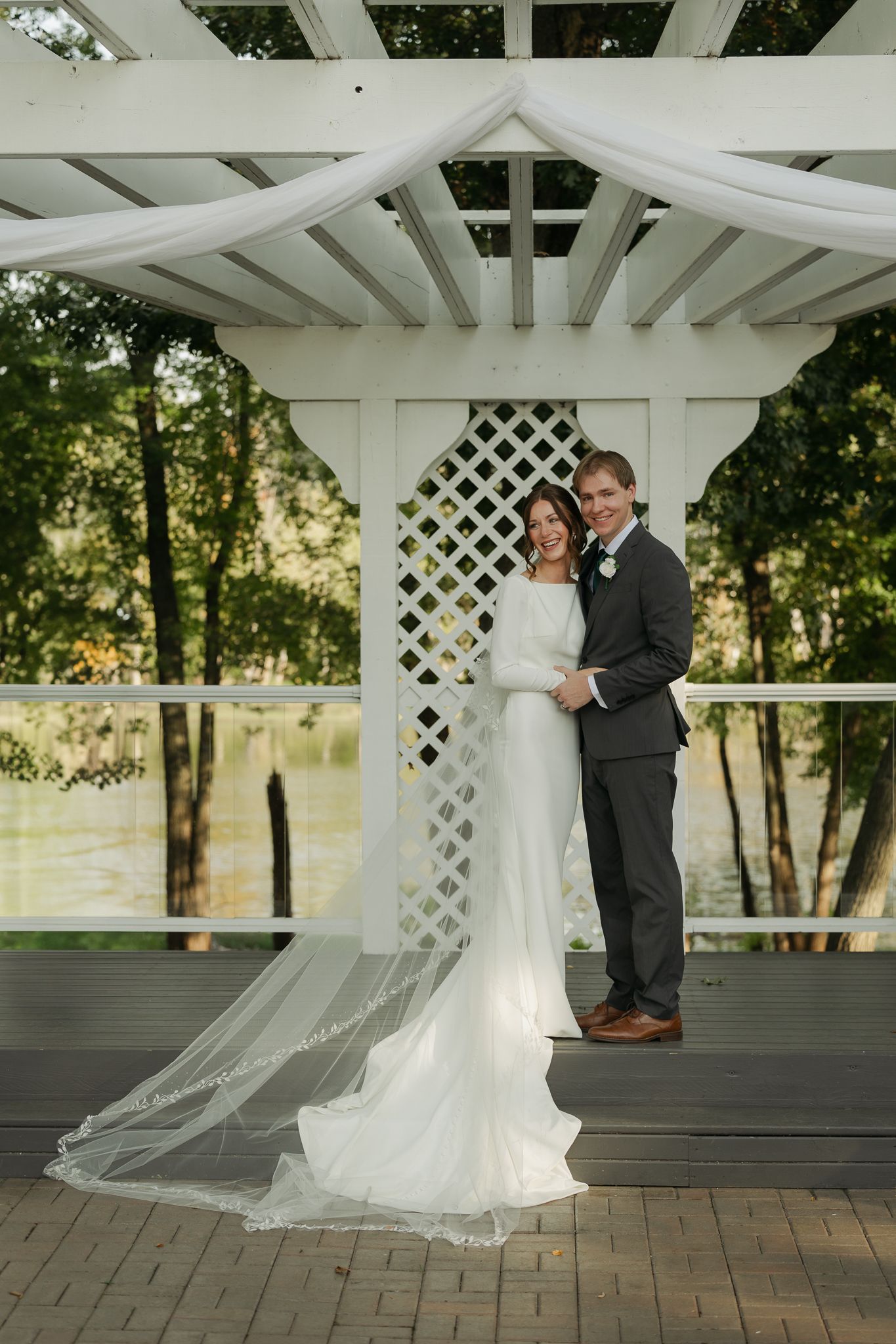 A couple shares an intimate moment under a white lattice gazebo during their wedding ceremony.