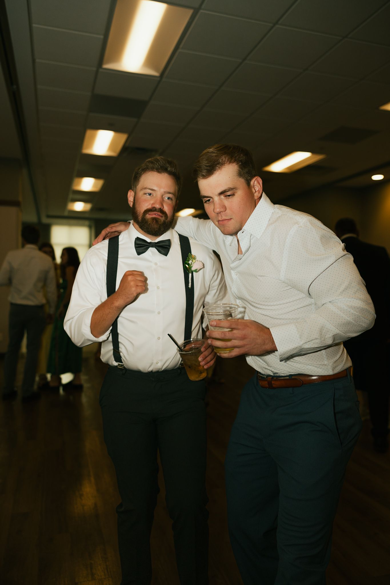 Two guests in formal attire sharing drinks at an indoor reception.