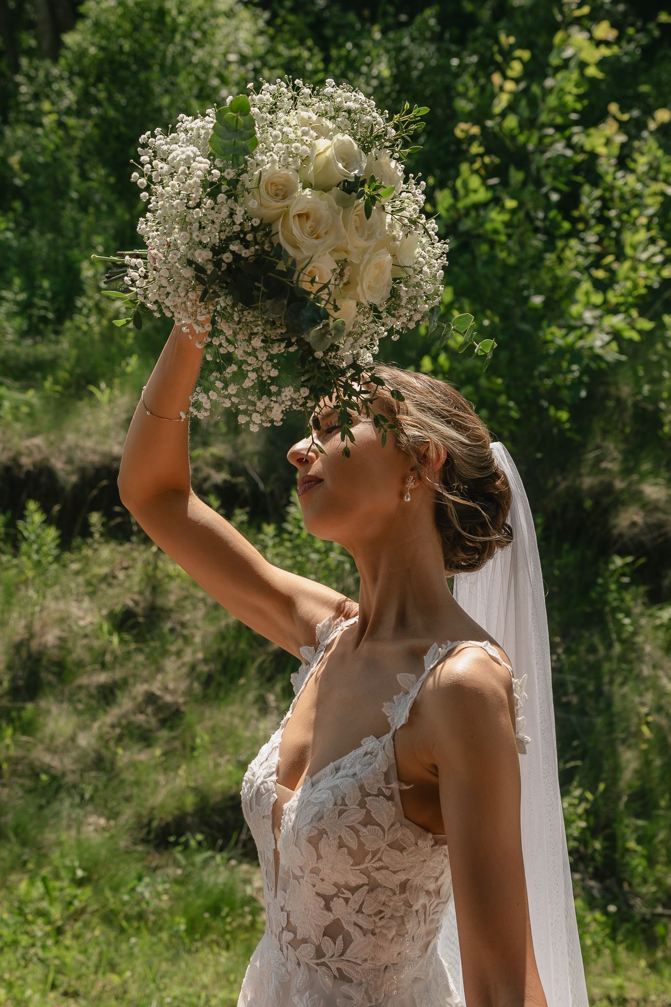 Bride wearing a delicate lace dress and flower crown poses in natural outdoor lighting.