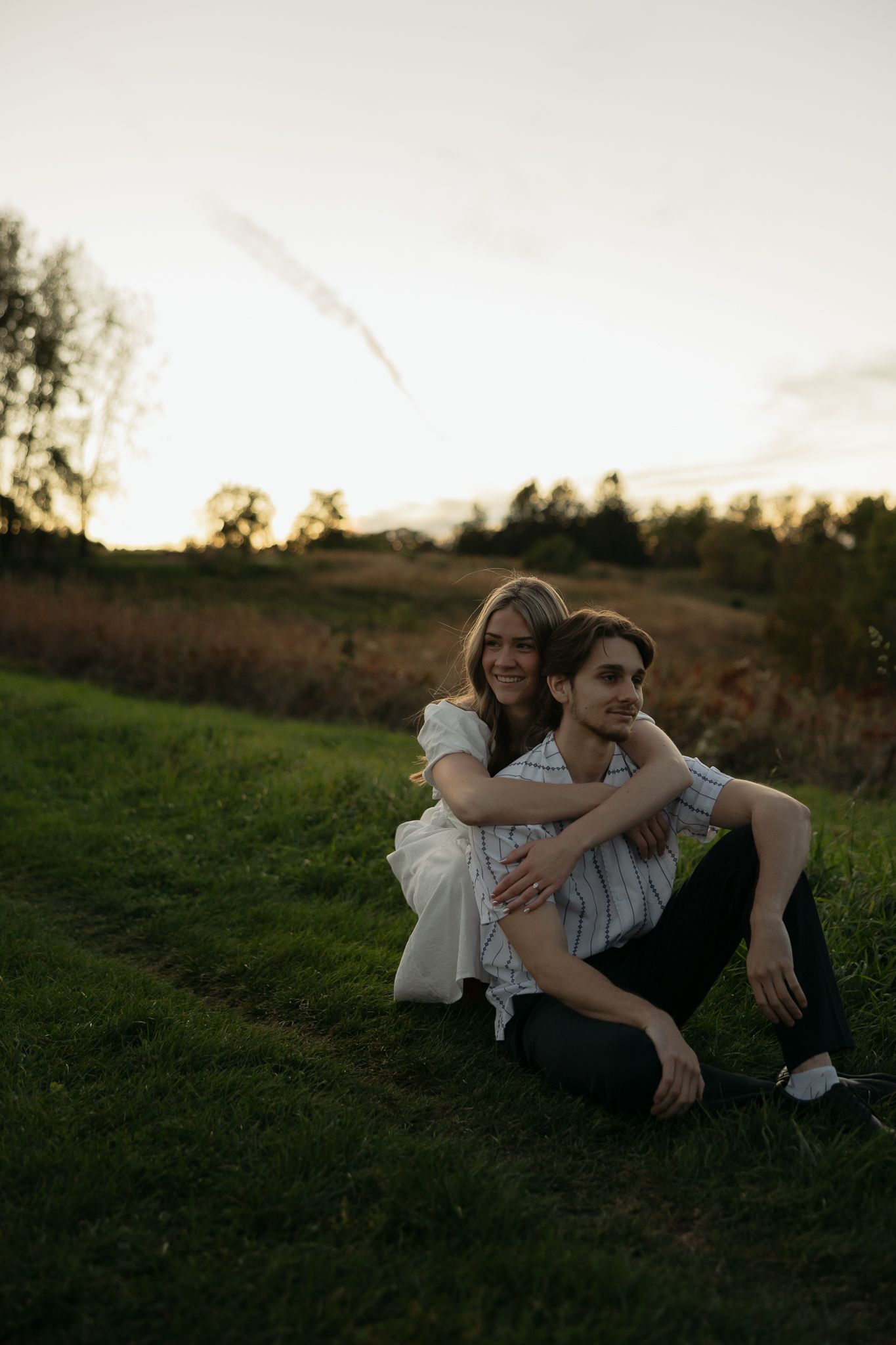 Two people lying together on grassy hill during golden hour.