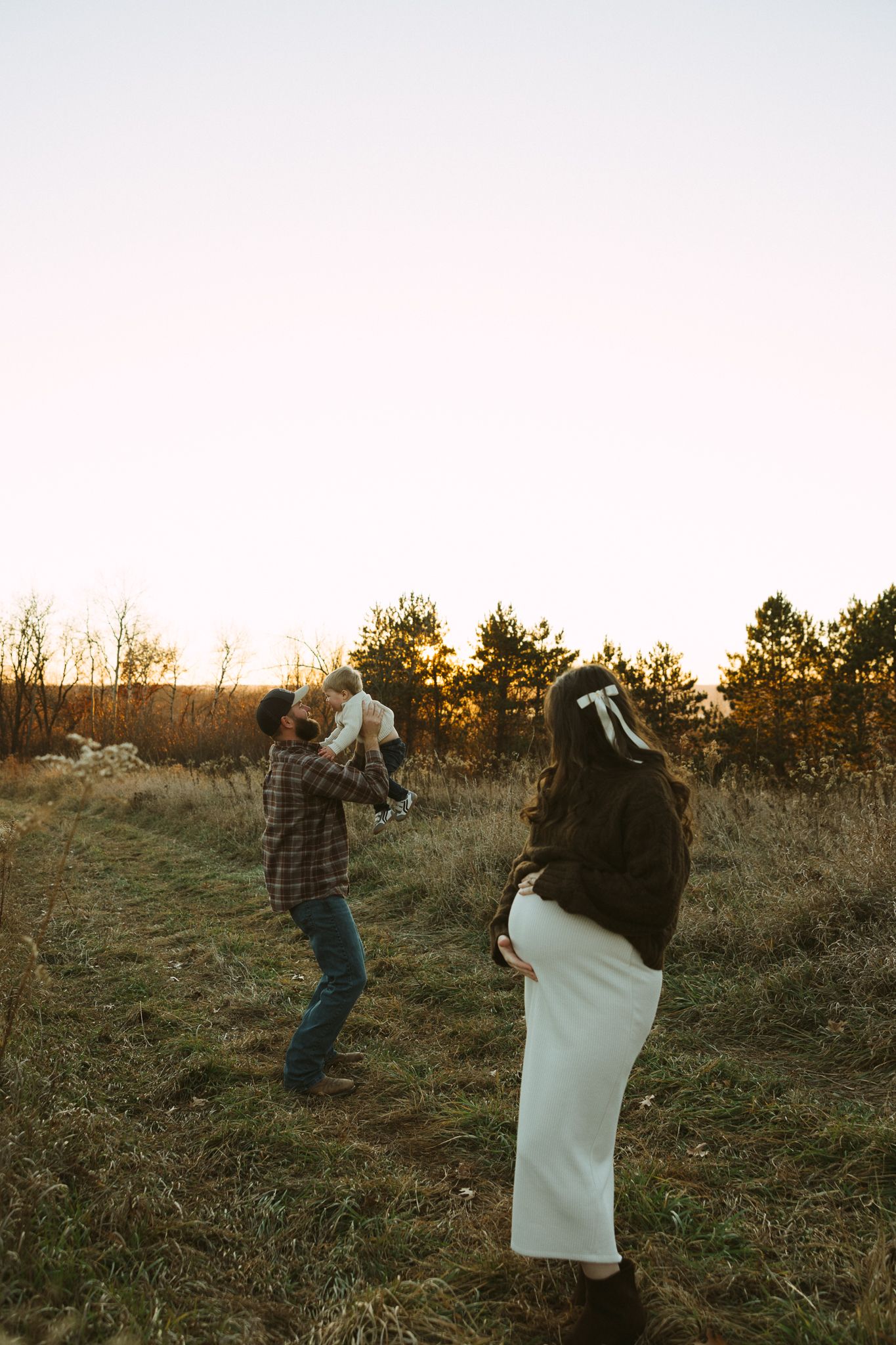 A playful pillow fight between two people takes place on a grassy hillside at sunset.