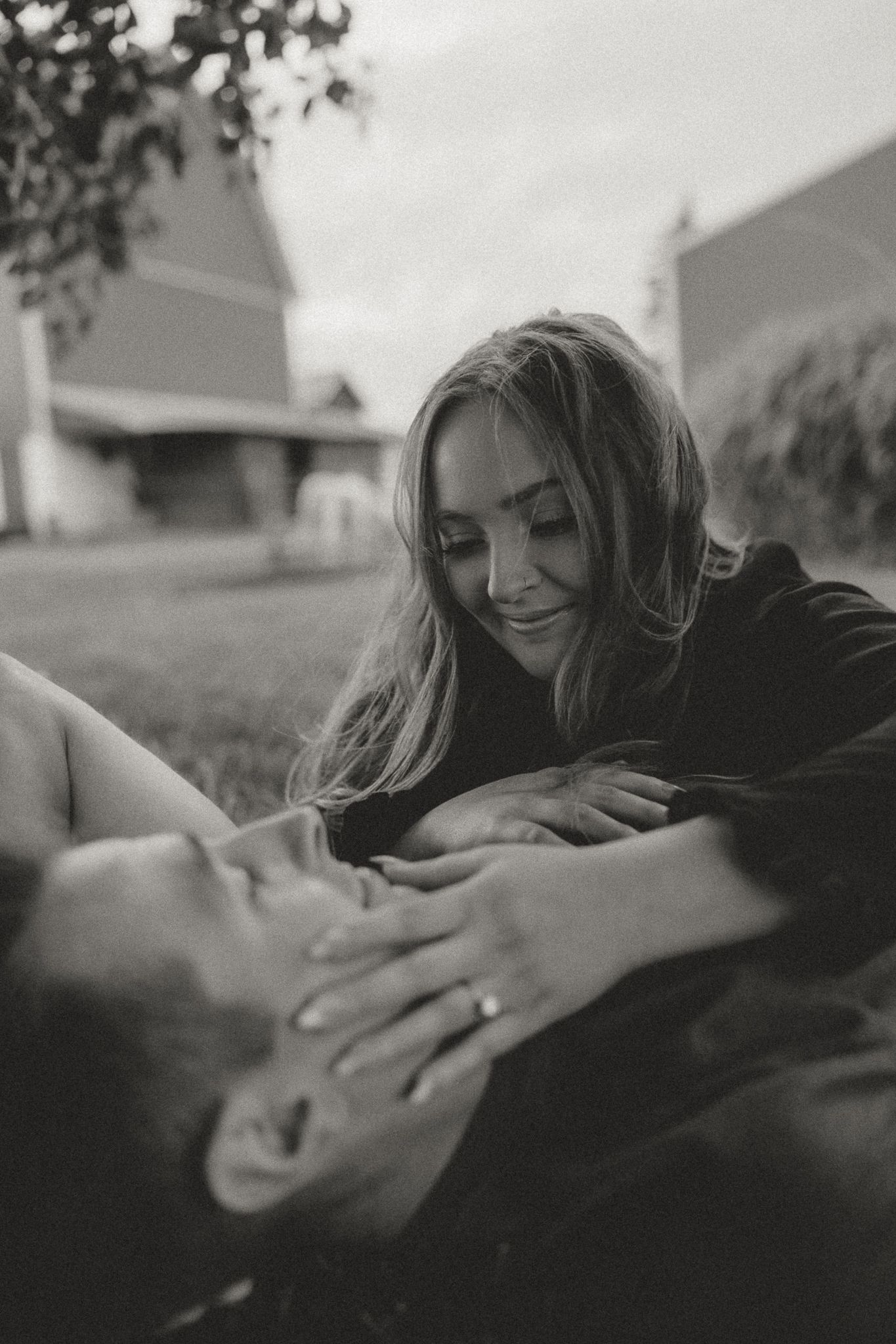 A black and white portrait captures an intimate moment between a couple on grass.