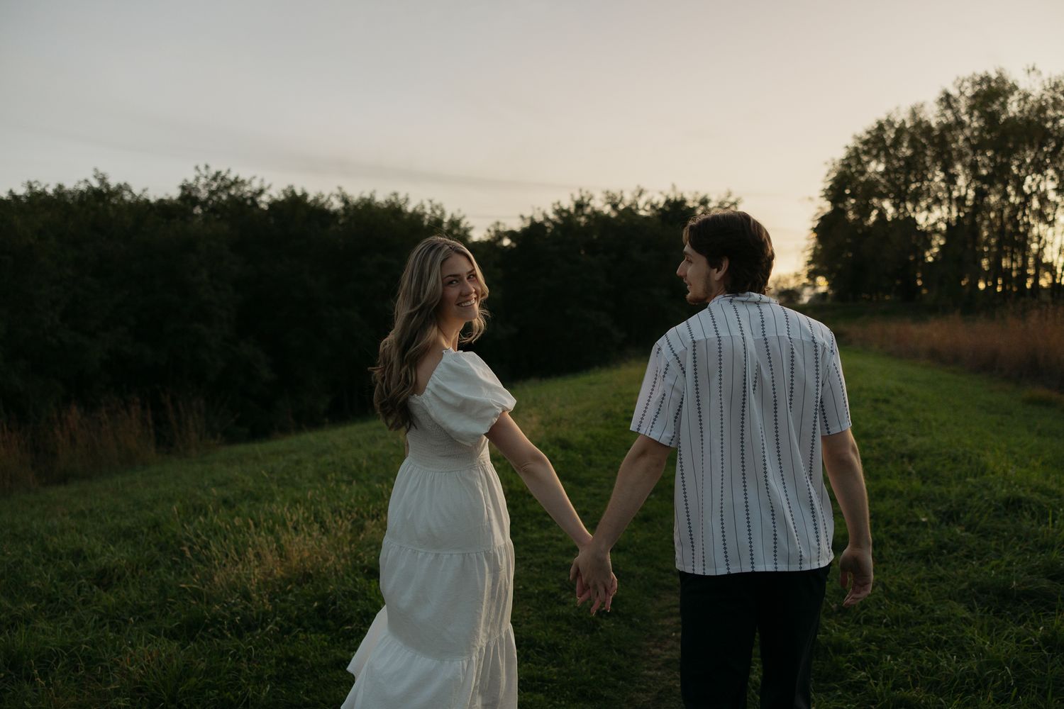 Silhouetted couple holding hands in a meadow at sunset.