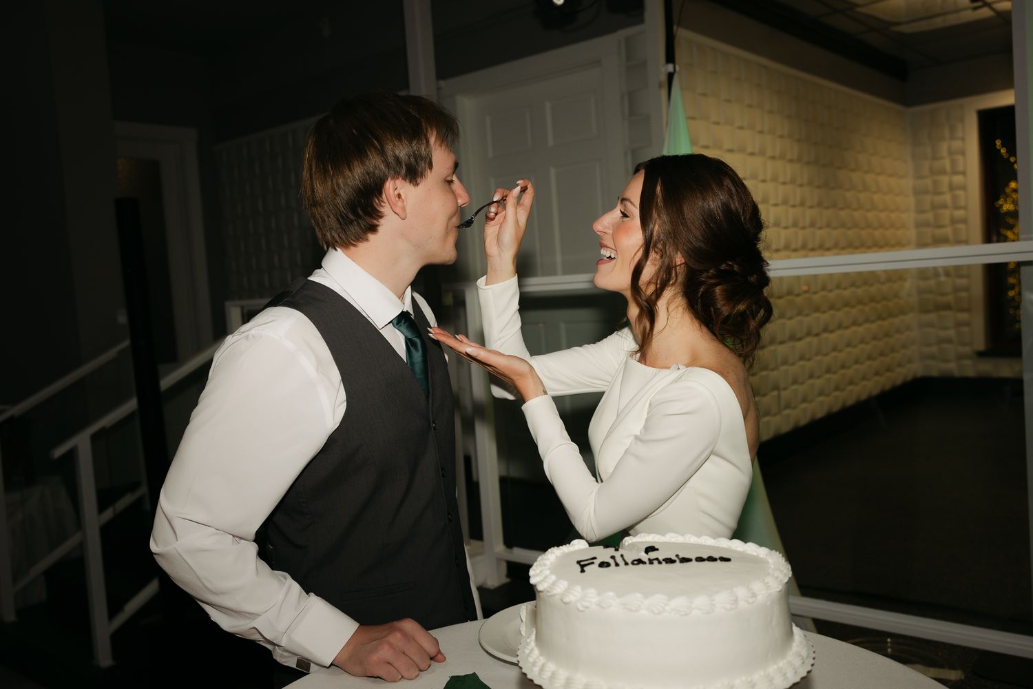 Newlyweds playfully feeding each other wedding cake.
