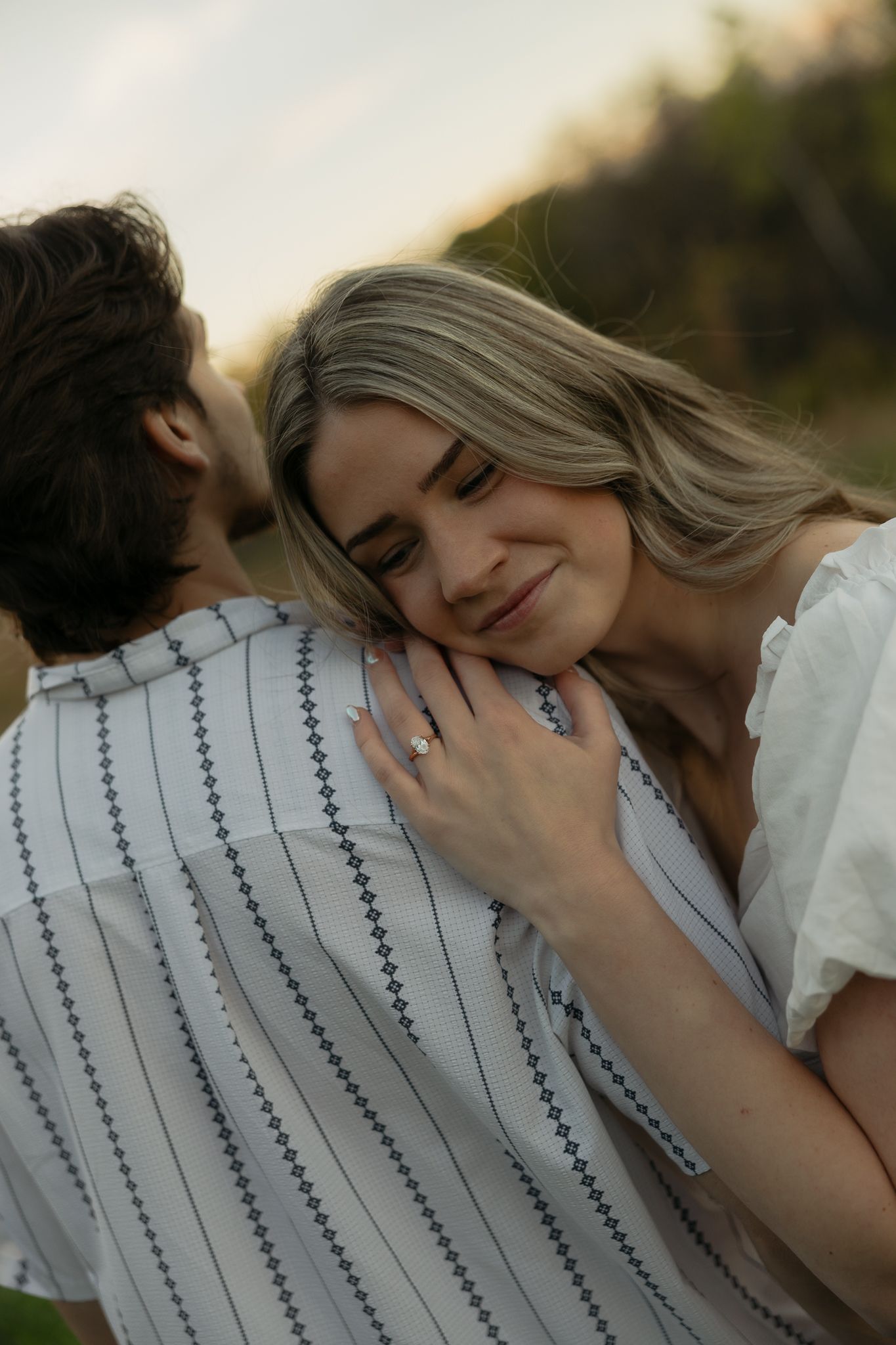 Intimate sunset portrait of couple sharing tender moment in striped shirt and white dress.