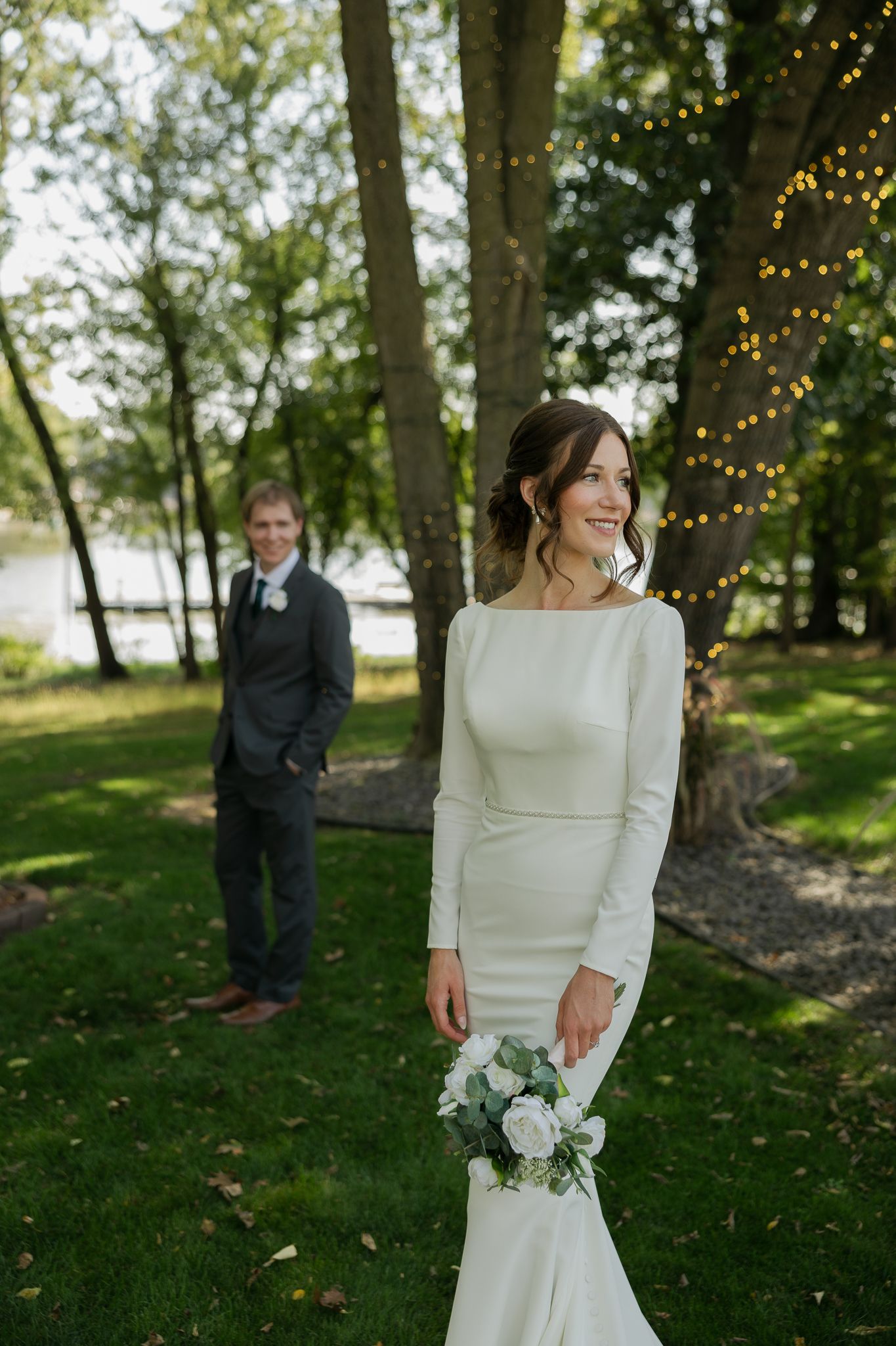 A bride in a classic white dress poses elegantly in a garden setting with string lights.