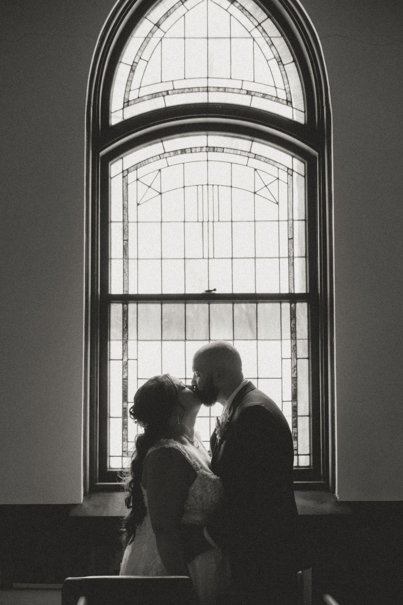 Silhouettes of figures standing by arched windows in a dimly lit room create a dramatic composition.