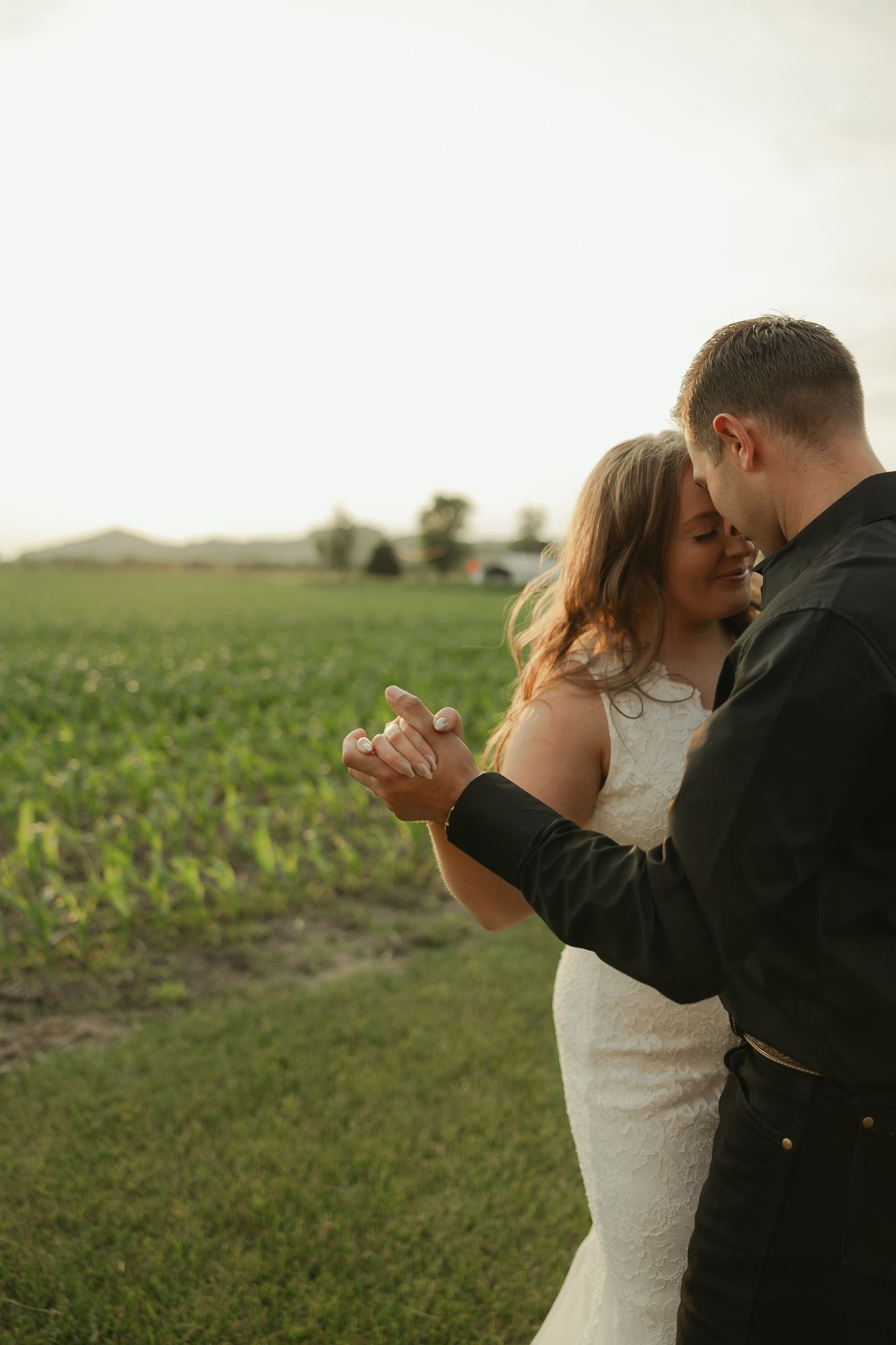 A couple dances together in a rural field during golden hour.